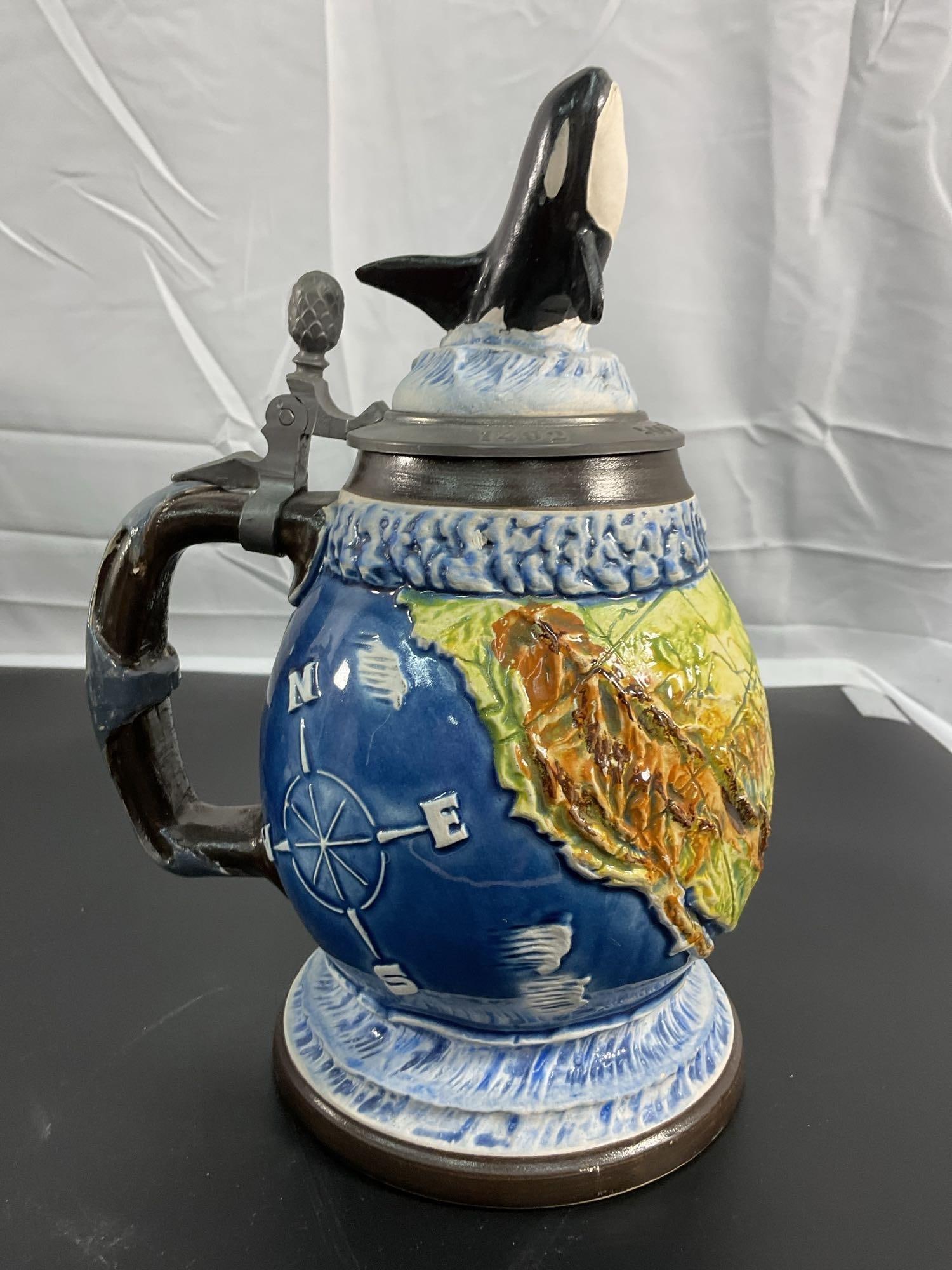 Limited Edition Orca Whale Themed Ceramic Beer Stein: This vibrant and detailed ceramic beer stein features an orca whale breaching from the lid, with a colorful relief of a world map and nautical motifs on the body. The stein is crafted in West Germany