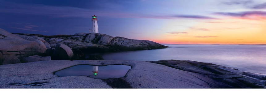 Lighthouse Reflection by Peter Lik (Australian, b.1959): Striking panoramic photograph by world-renowned landscape photographer Peter Lik, capturing a tranquil coastal scene at sunset. A solitary lighthouse stands on rugged rocks, its reflection perfectly m