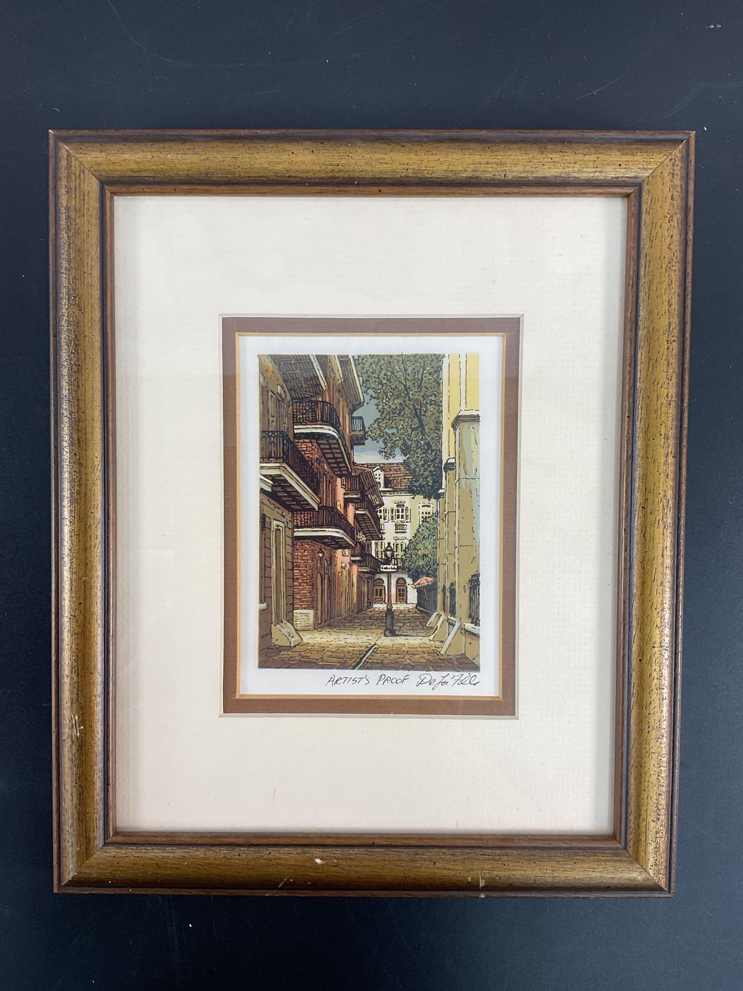 Paul De La fille (American, 1927-2010) Lithograph: This is a framed and matted print titled "Pirate's Alley" depicting a charming street scene in New Orleans. The artwork captures the historic architecture, ornate iron balconies, and cobblestone pathw