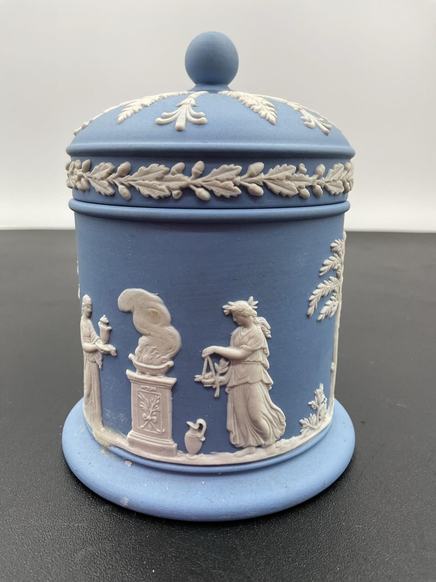 Wedgwood Jasperware Lidded Jar in Blue and White: This is a classic piece of Wedgwood Jasperware, a neoclassical-style lidded jar featuring matte blue stoneware with applied white relief decorations. The design showcases Greco-Roman figures and trees