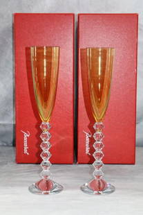 Exquisite Pair of Baccarat Crystal Champagne Flutes: A pair of elegant Baccarat Vega Flutissimo champagne flutes in amber crystal, featuring a sleek elongated bowl and a bold geometric stem composed of stacked diamond-shaped crystal segments. Designed f