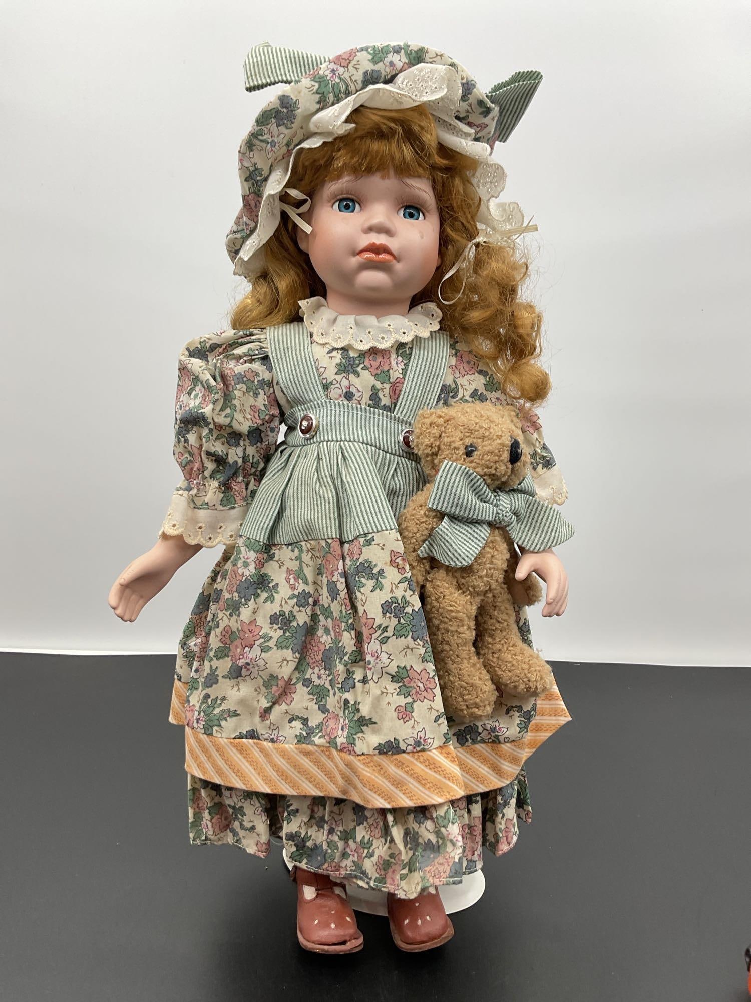 Porcelain Doll in Floral Dress with Tear Drop and Teddy Bear: This unique porcelain doll features auburn hair, blue eyes, and a lifelike teardrop on her cheek, giving her a sorrowful expression. She is dressed in a vintage-style floral print dress with puffed sl