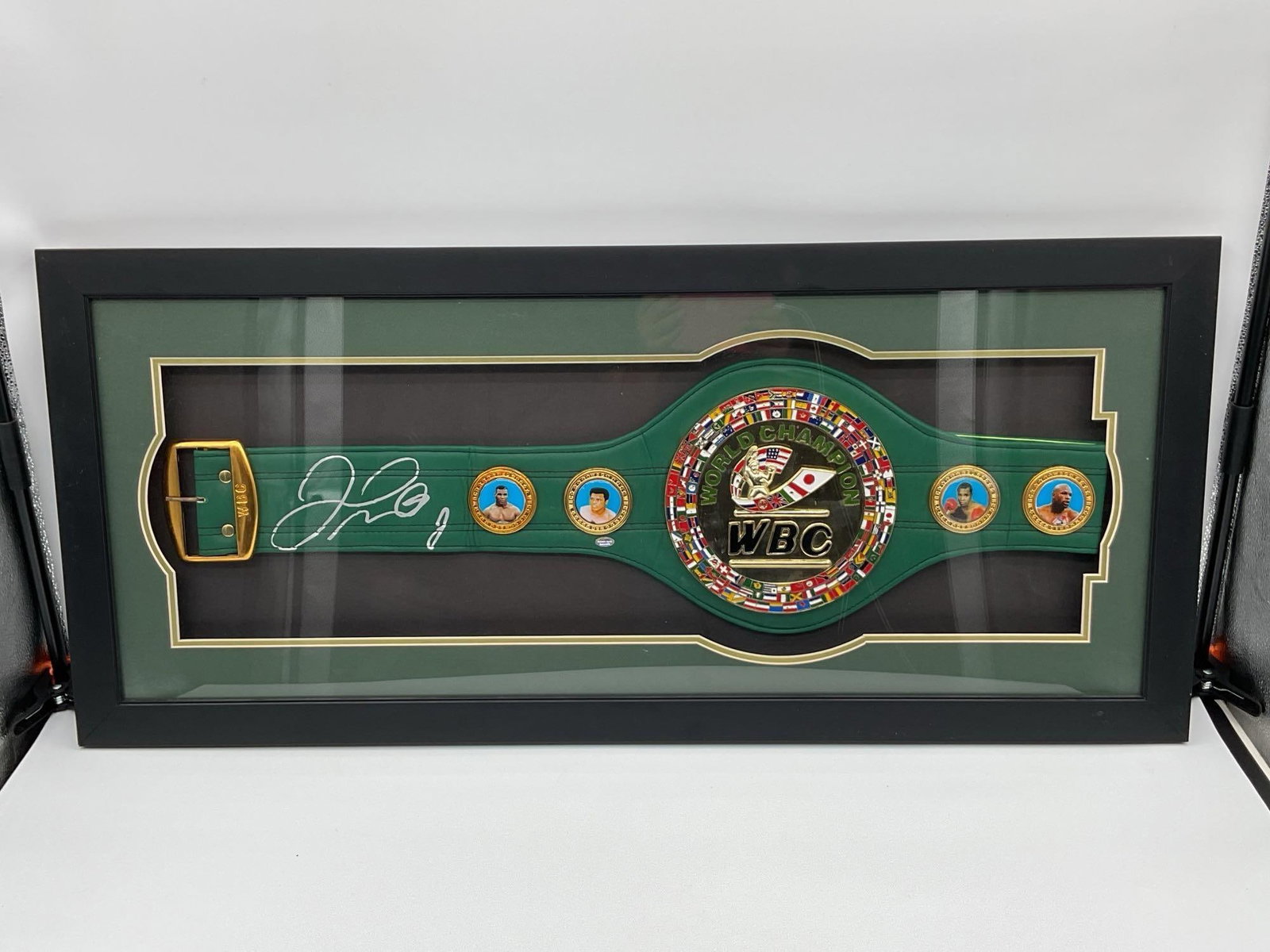 WBC World Championship Belt Display: Framed display of an official-style World Boxing Council WBC World Championship belt, featuring vibrant colors, gold detailing, and national flags encircling the central medallion. The green leather s