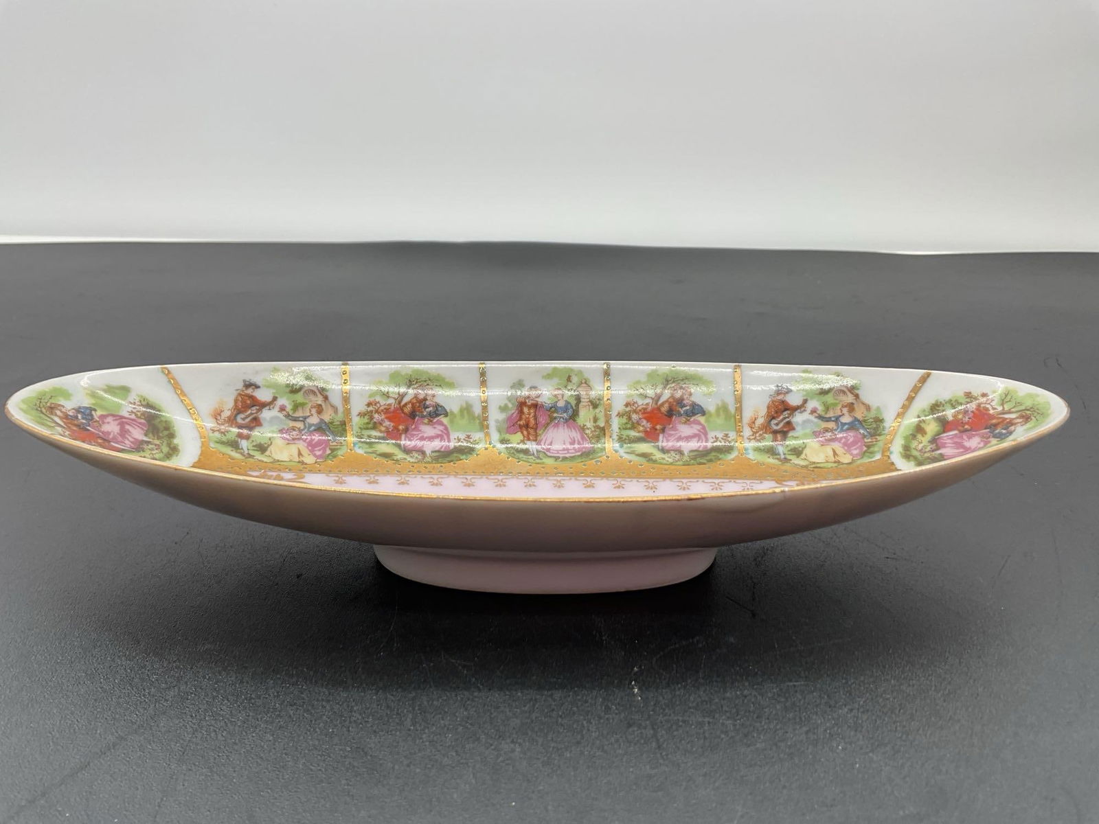 Vintage Romantic Courting Scene Porcelain Dish: This oval porcelain dish features a series of romantic 18th-century-style courting scenes around the border, with couples dressed in period attire, surrounded by greenery and soft pastel colors. The c