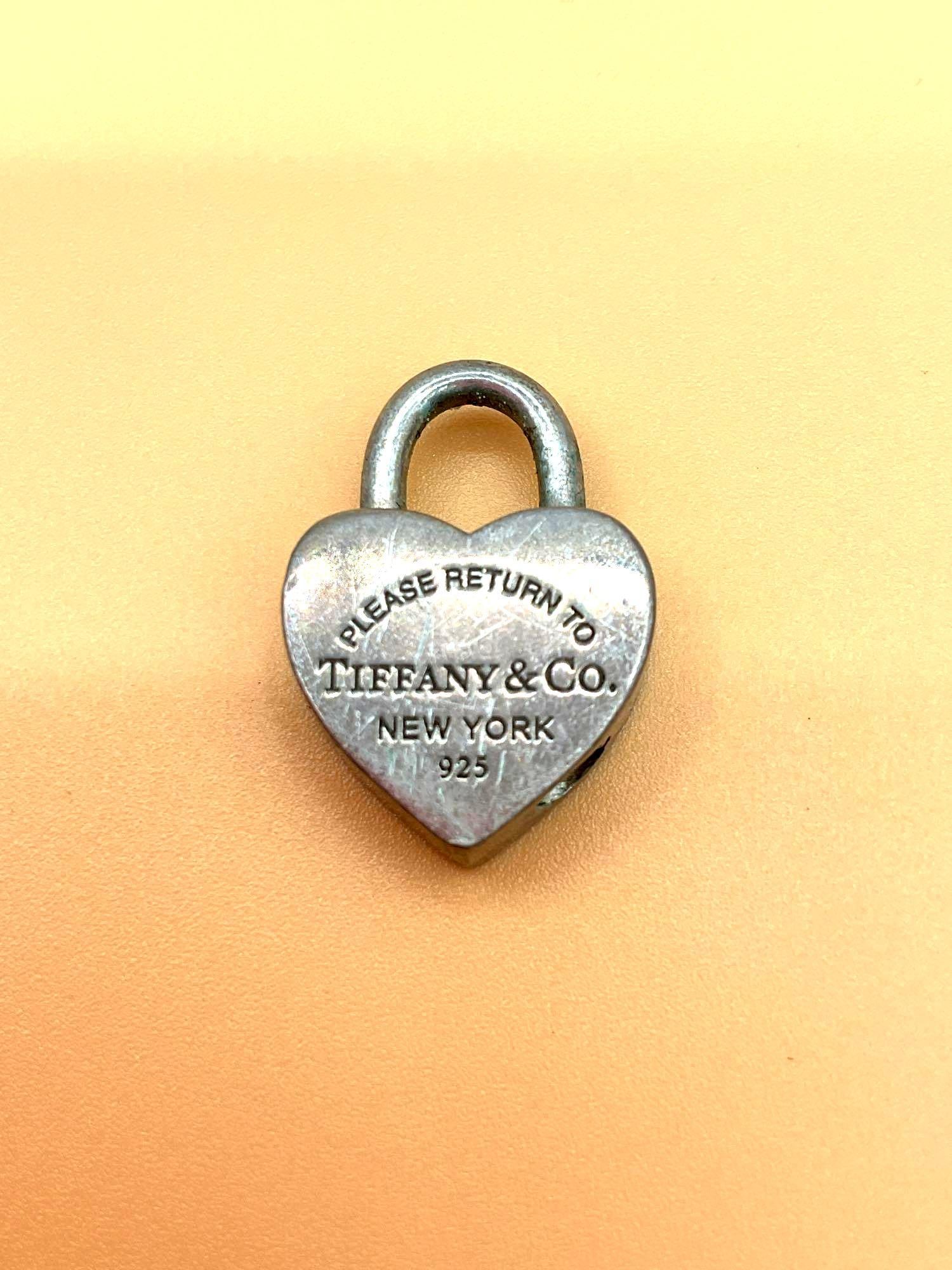 Tiffany & Co. Sterling Silver Heart Lock Charm: This is a heart-shaped charm or pendant by Tiffany & Co., designed to resemble a miniature padlock. Made of sterling silver, it features the iconic “Tiffany & Co.” branding along the e