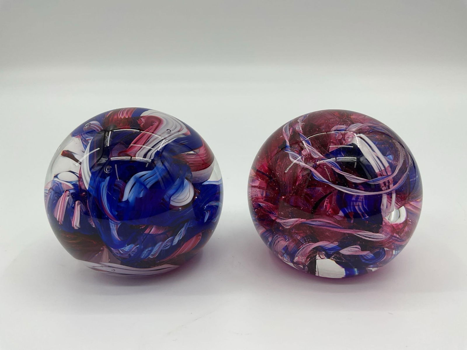 Hand-Blown Art Glass Paperweights: A pair of vibrant hand-blown art glass paperweights, each featuring swirling colors encased in clear glass. One exhibits a patriotic mix of blue, red, and white, while the other showcases shades of pi