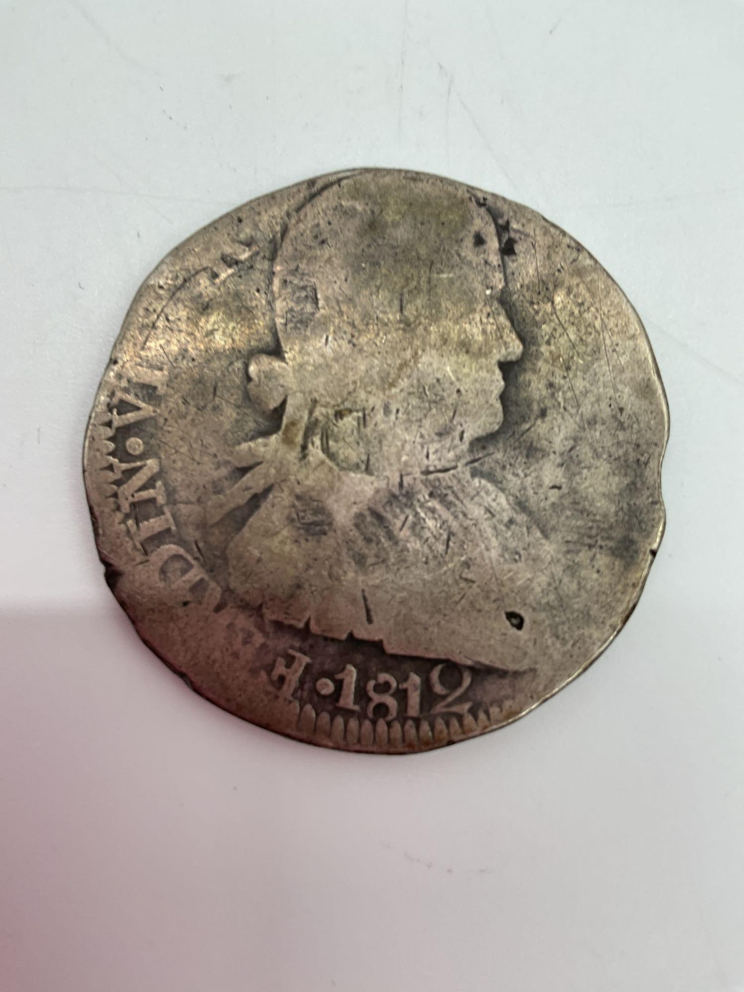 1812 Spanish Colonial Silver 8 Reales Coin: Heavily worn 8 Reales silver coin dated 1812, featuring a partial portrait of King Ferdinand VII on the obverse with the inscription “HISPAN ET IND REX.” The reverse shows remnants of the crow