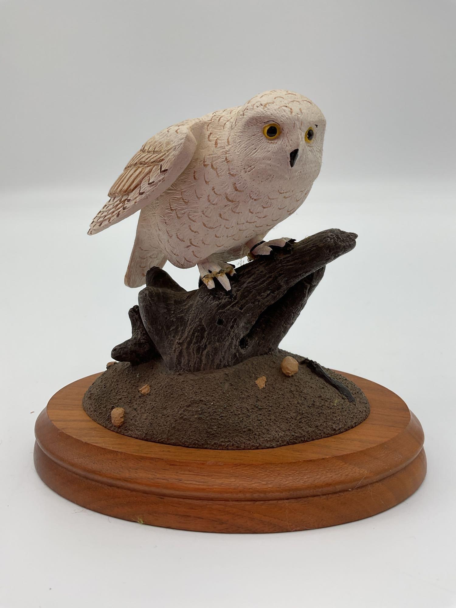 Snowy Owl, Original Sculpture by James E. Dikon Jr.: A beautifully crafted snowy owl figurine, perched on a textured branch. The owl features intricate feather detailing with subtle brown accents on its white plumage and sharp yellow eyes that give it a