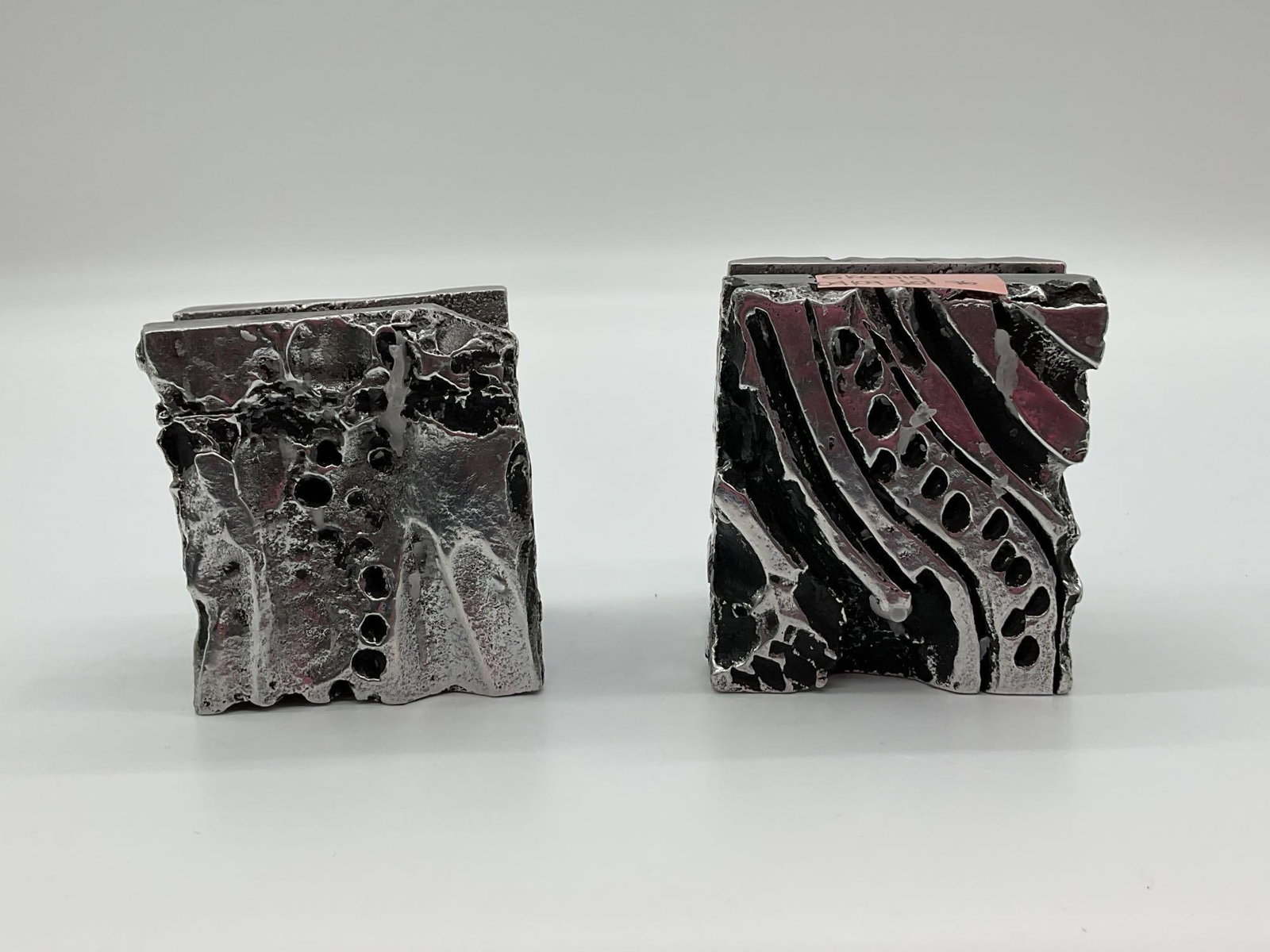 Pair of Abstract Brutalist Metal Candle Holders - Artist Unknown: A pair of robust and heavily textured Brutalist-style candle holders, crafted from metal with a striking abstract design. These holders showcase an expressive, raw aesthetic marked by rough surfaces a