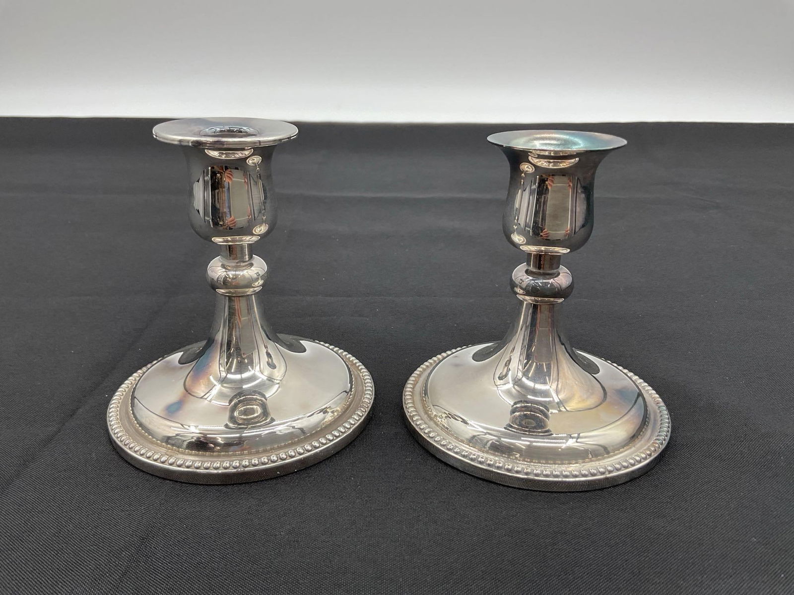 Pair of Silver-Plated Beaded Edge Candlesticks by Kotum: This is a pair of elegant silver-plated candlesticks with a flared lip and rounded base featuring a beaded edge design. The reflective surface and classical shape suggest they are mid to late 20th cen