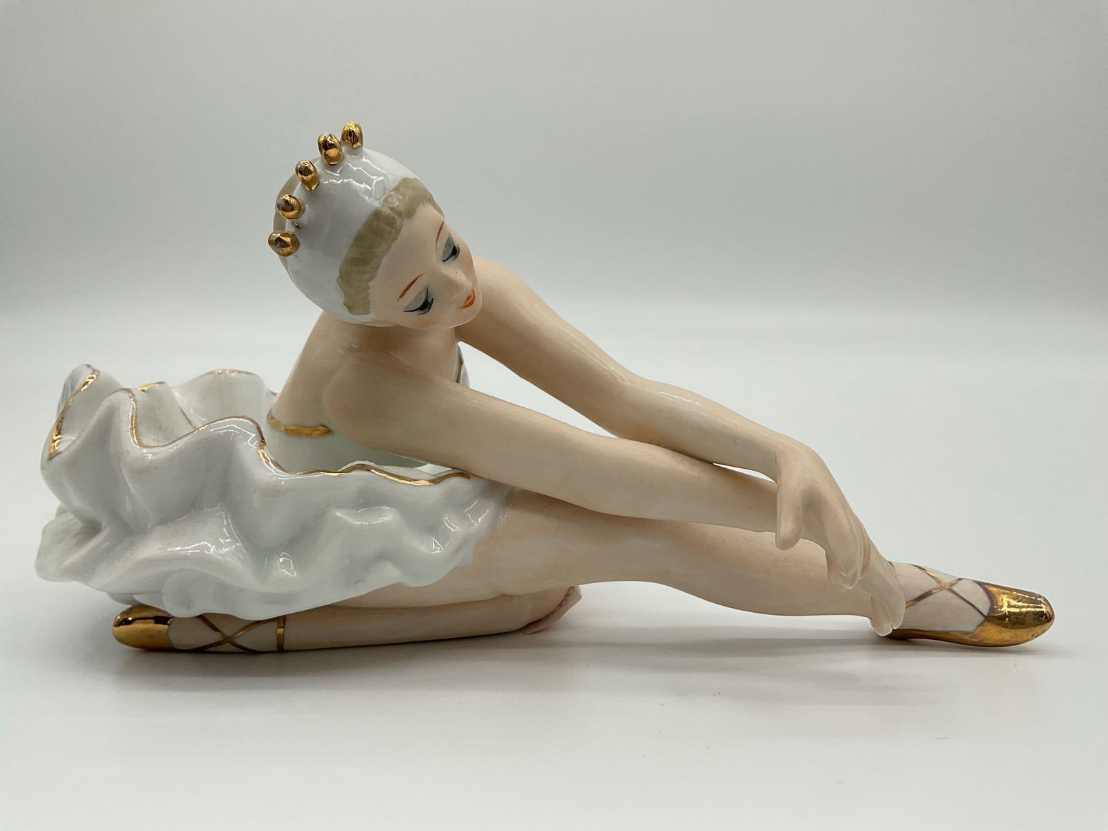 Monti Pierro Designed in Spain Porcelain Ballerina Figurine: Elegant porcelain figurine by Monti Pierro, depicting a ballerina seated and adjusting her golden ballet slipper. Beautifully detailed with a white ruffled tutu accented by fine gold highlights. Marke