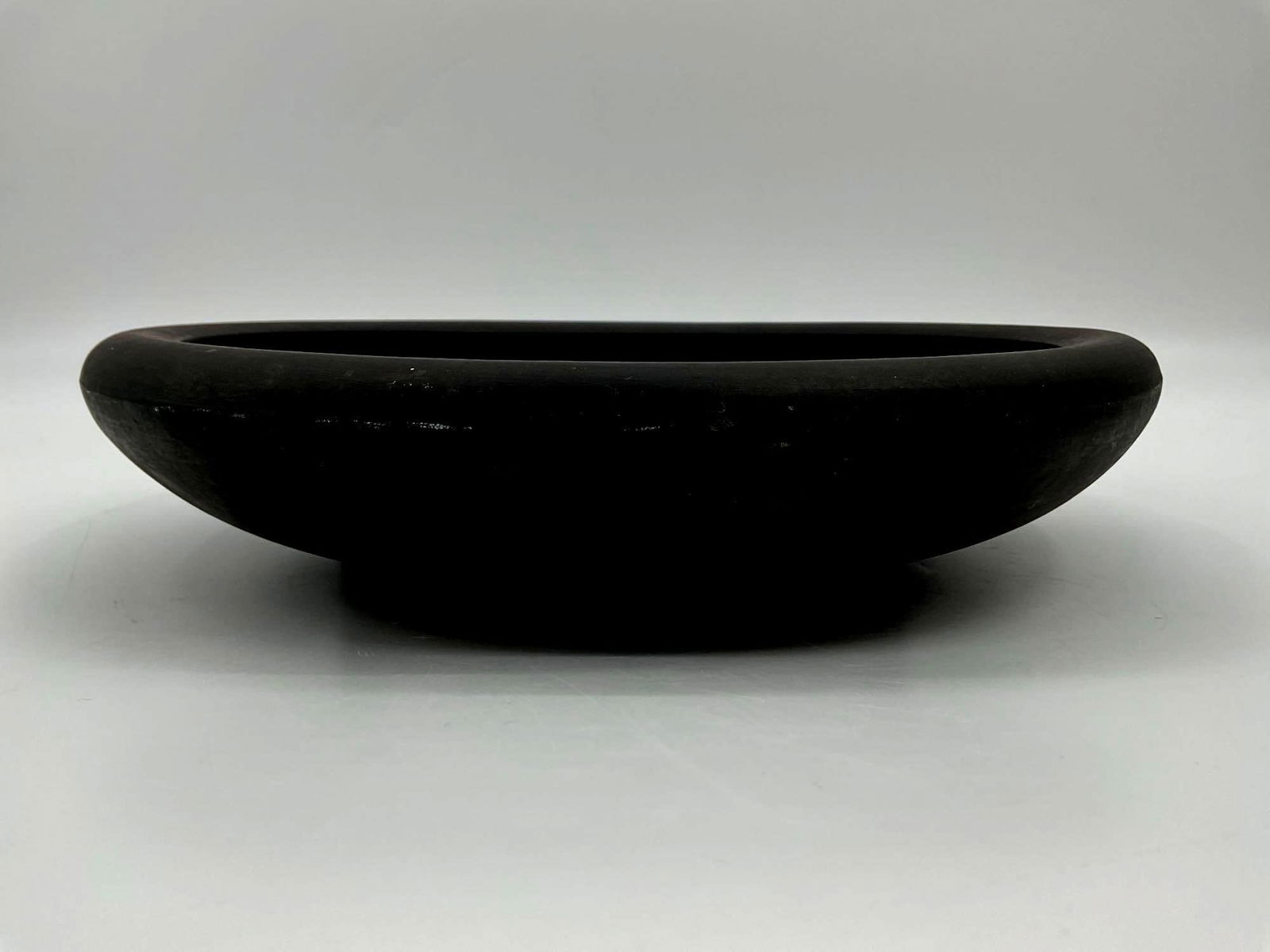 Wedgwood Black Basalt Round Tray: A minimalistic black basalt tray by Wedgwood featuring a thick, raised rim and smooth flat interior. This piece reflects the elegant simplicity of 18th century English neoclassical stoneware design. D