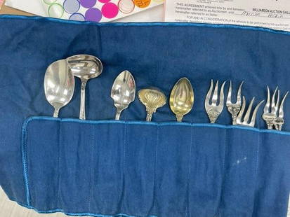 2 Antique/Vintage Silver Flatware Sets: This is a mixed set of antique or vintage silver flatware, carefully stored in fabric rolls for preservation. The set includes: Various serving spoons, some with ornate shell patterns Four-tine forks