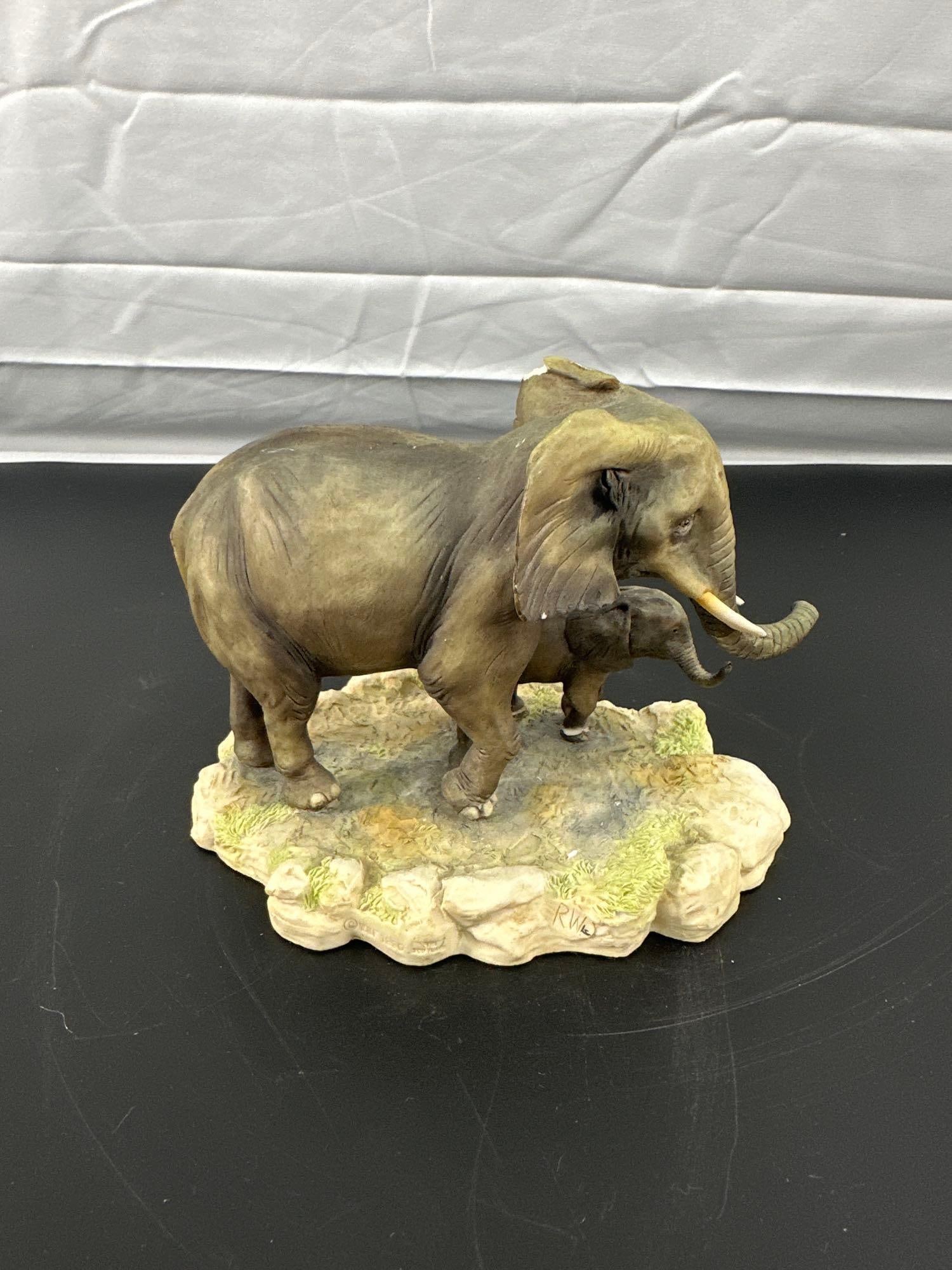 Capodimonte-Style Porcelain Elephant Figurine with Calf: This is a finely crafted porcelain figurine depicting a lifelike elephant and its calf walking across a naturalistic base. The piece features detailed texturing and realistic shading, capturing the ge