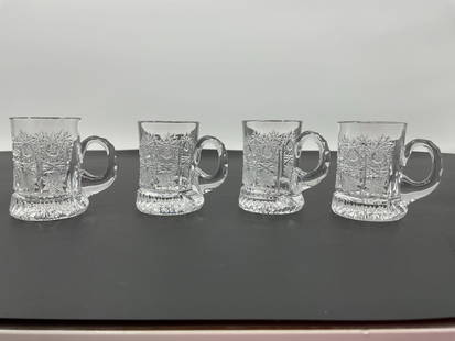 Set of Four Cut Crystal Glass Mugs: A set of four small crystal glass mugs featuring an intricate cut-glass design with geometric and floral motifs. The handles are smoothly integrated into the design, and the base has a starburst patte