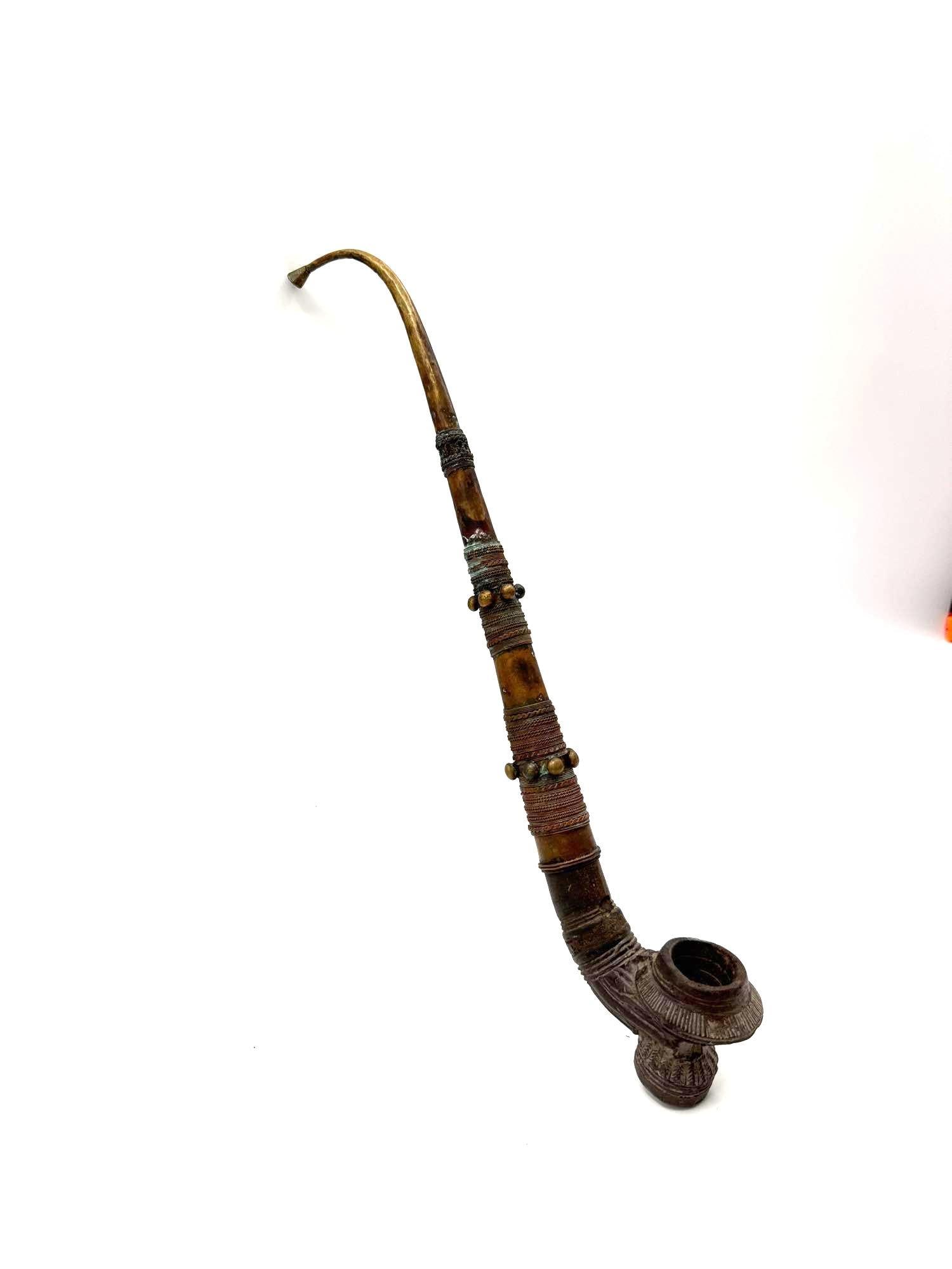 African Tribal Ceremonial Pipe: Ornate tribal pipe featuring a curved stem, textured carved patterns, and wrapped accents with colored threads and beads. Medium: Carved wood, metal, beads, and thread