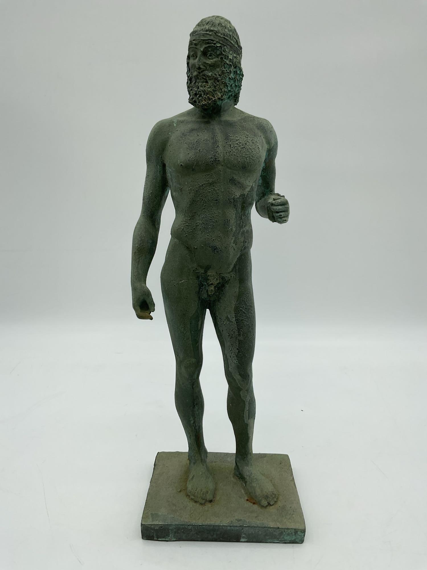 Greek Warrior Bronze Replica Statue: Small verdigris-finished bronze or composite statue of a bearded nude male figure wearing a helmet, modeled after classical Greek sculptures like the Riace Bronzes. The stance and stylized musculature