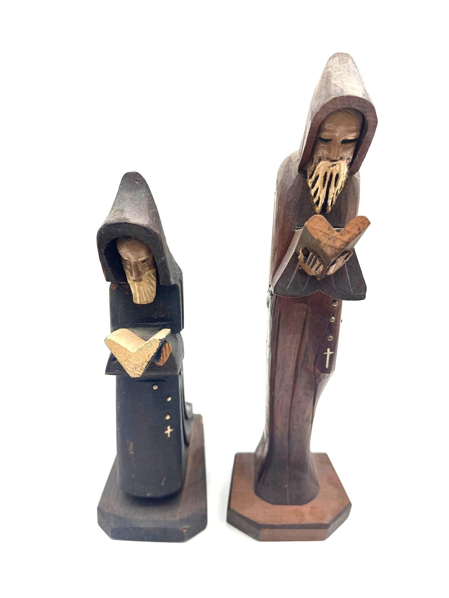 Hand-Carved Wooden Monk Figurines – Set of Two: Pair of tall, slender wood carvings depicting monks in hooded robes reading books. Both figures feature bearded faces and carved rosaries with cross details, each crafted with subtle stylistic variati