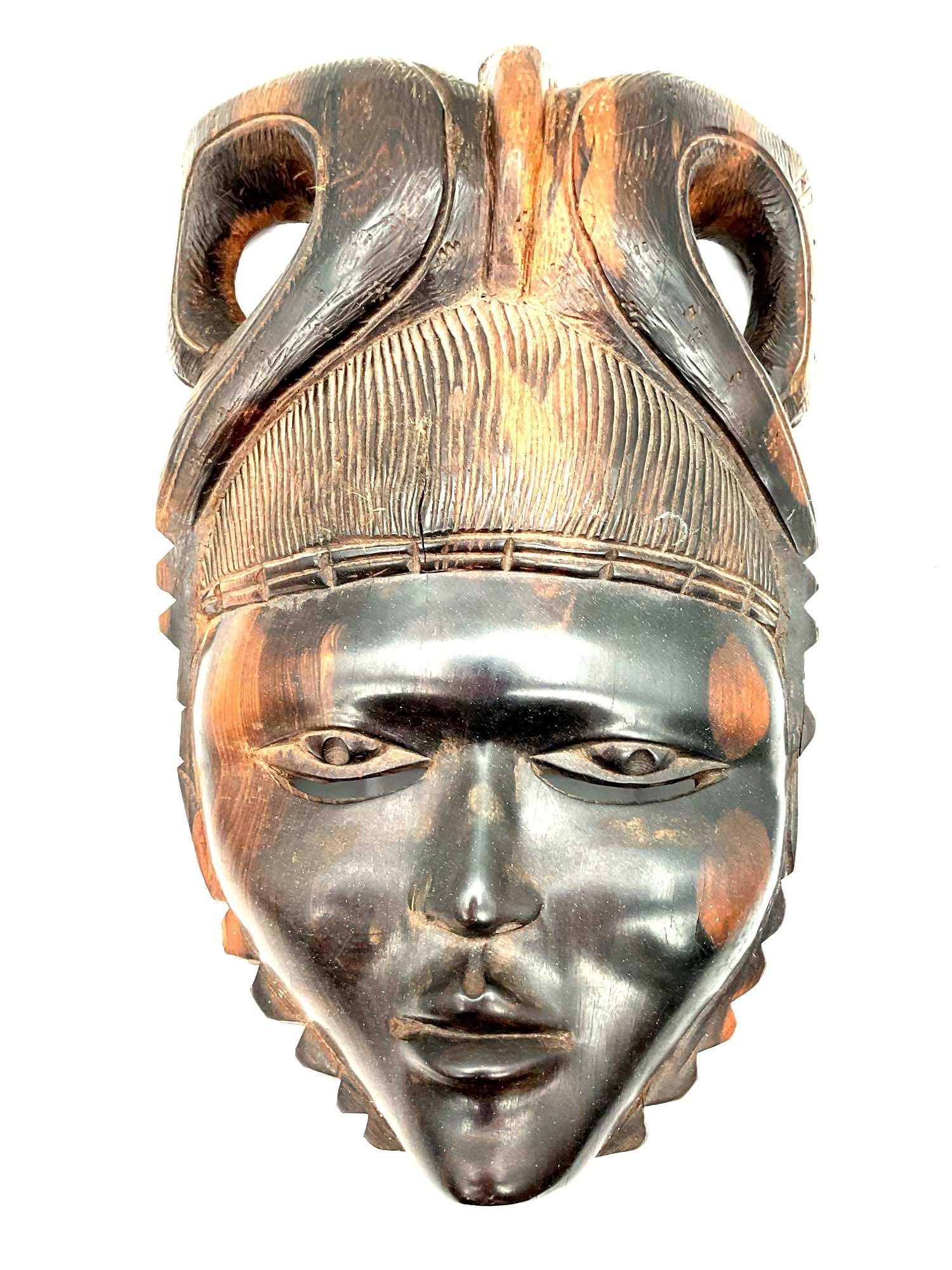 Hand-Carved African Tribal Mask: This is a traditional African tribal mask, likely originating from West Africa. The mask features a serene, elongated face with high cheekbones, a narrow chin, and detailed carvings on the headdress. 