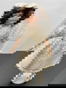 Porcelain Doll in White Bridal Dress with Veil: This porcelain doll has curly brown hair, a gentle smile, and brown eyes. She is dressed in a satin-like white dress with lace bodice detailing and puffed sleeves, finished with a ribbon flower at the