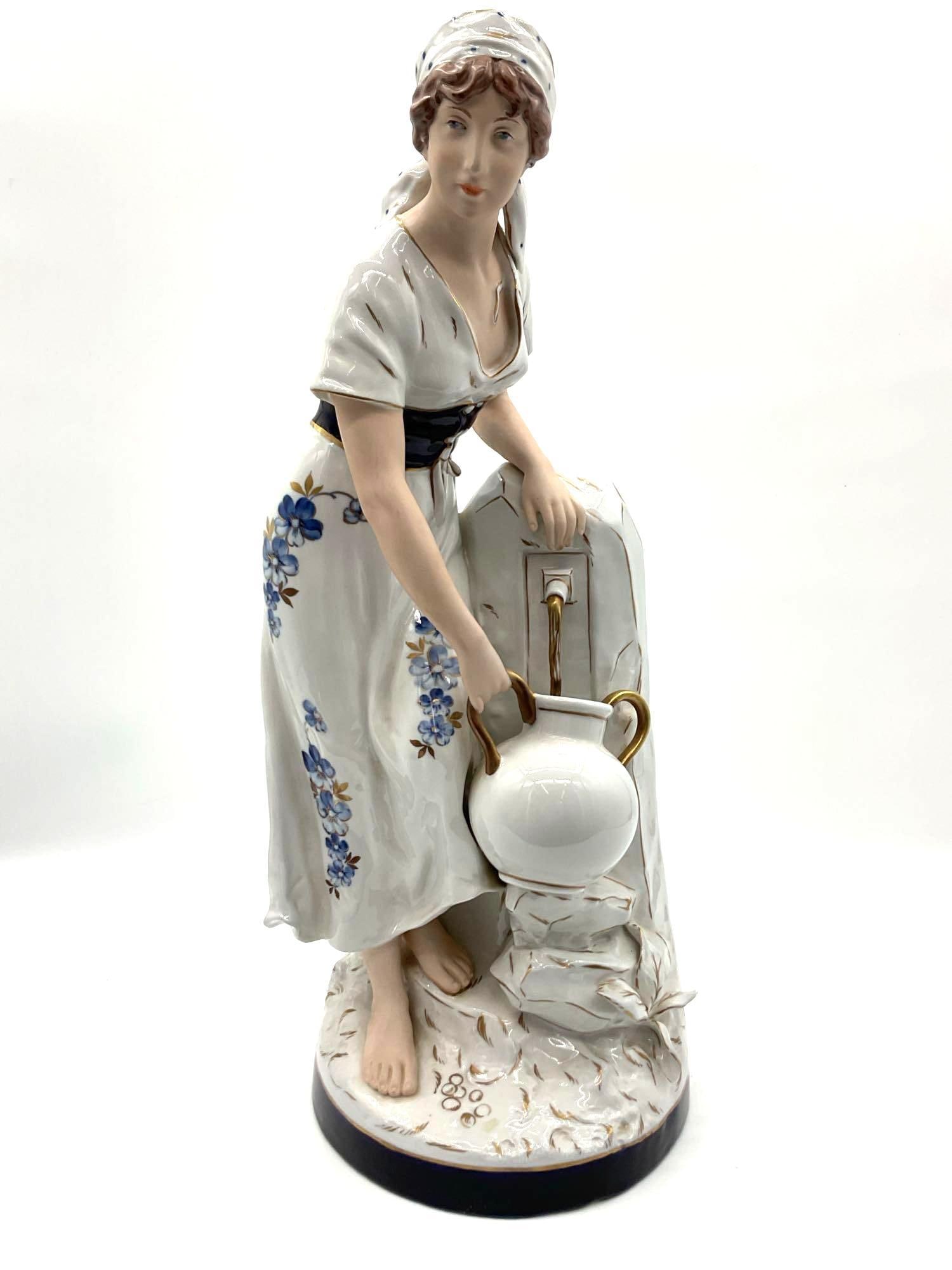 Royal Dux Bohemian Porcelain Figure: Finely detailed porcelain sculpture of a barefoot young woman in a floral-patterned dress and headscarf, leaning on a rock while holding a white double-handled jug with gold accents. The figure featur