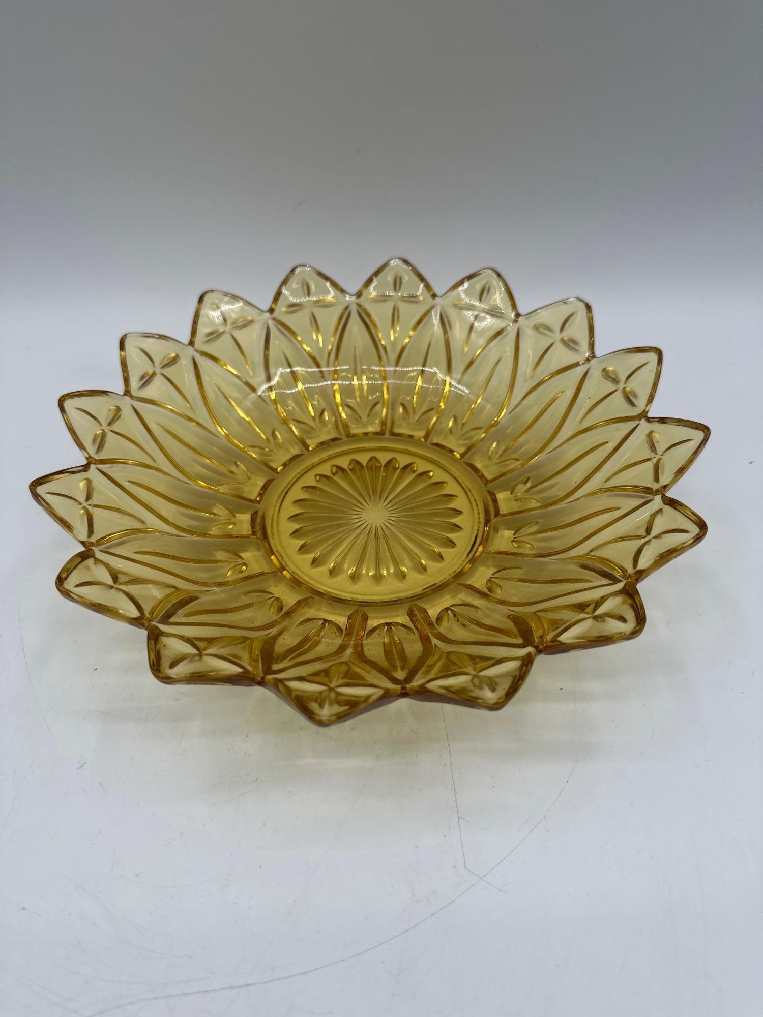 Amber Pressed Glass Sunburst Bowl: Description: Decorative amber-colored glass bowl featuring a detailed sunburst and petal pattern, ideal for serving or display. Dimensions: H:2.5in L:10in W:10in