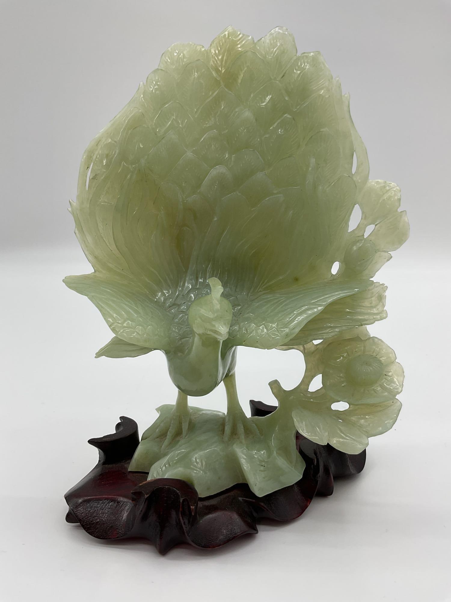 Carved Green Jade Peacock Sculpture on Wooden Stand: A beautifully detailed sculpture depicting a peacock intricately carved from pale green jade. The piece captures fine feather textures, floral accents, and graceful elegance. It rests upon a polished