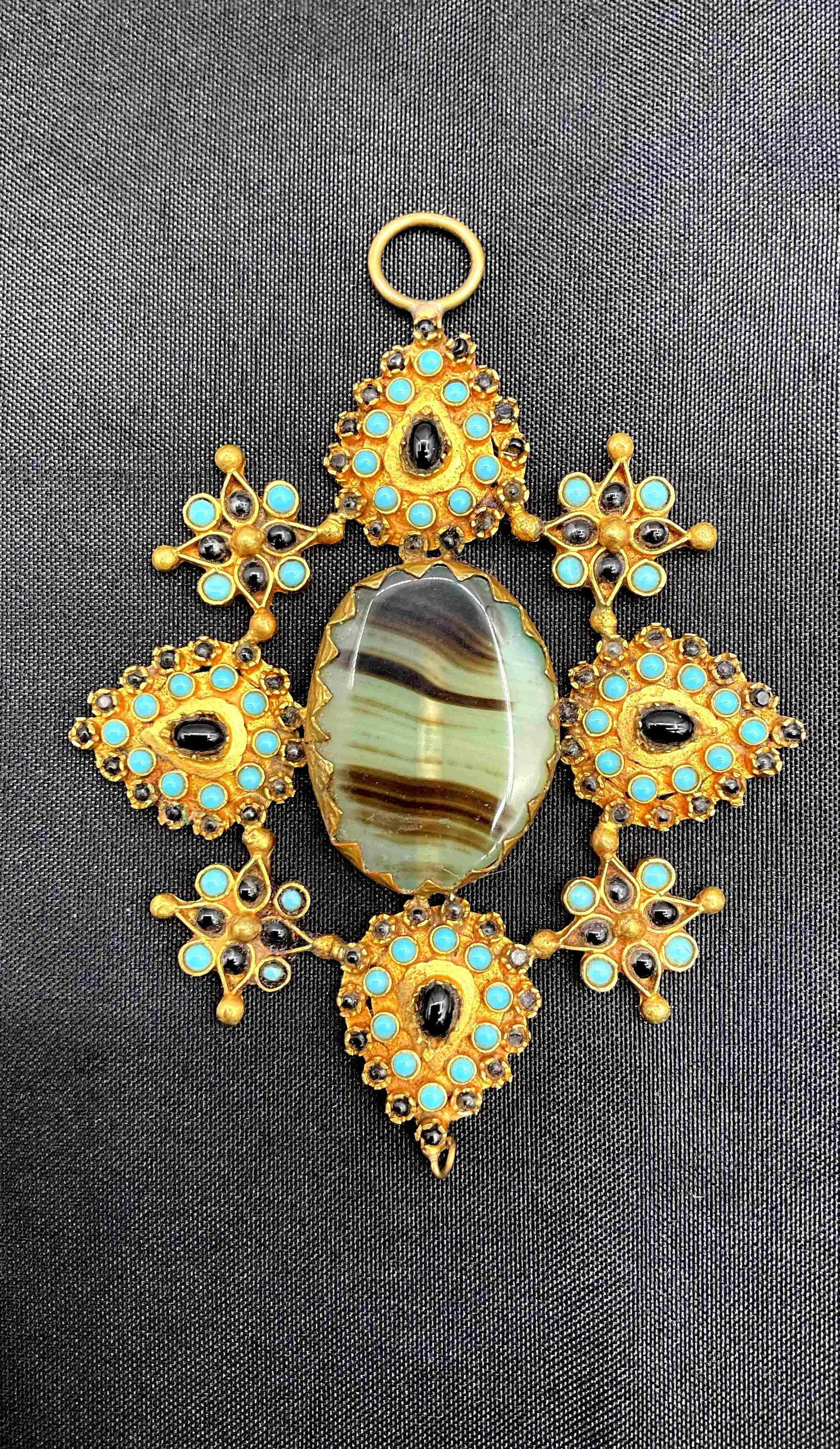Ornate Vintage-Style Pendant: Large gold-tone filigree pendant with turquoise bead accents and central oval cabochon stone, presented in a decorative pink mesh bag Medium: Metal, beads, and cabochon stone Dimensions: L4in W3in