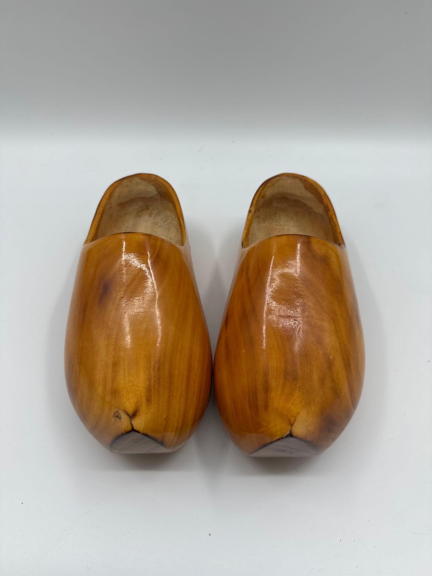 Pair of Traditional Dutch Wooden Clogs: A polished pair of handcrafted wooden clogs, traditionally worn in the Netherlands. These shoes feature a smooth, curved form with natural wood grain and light varnish. Medium: Carved and polished woo