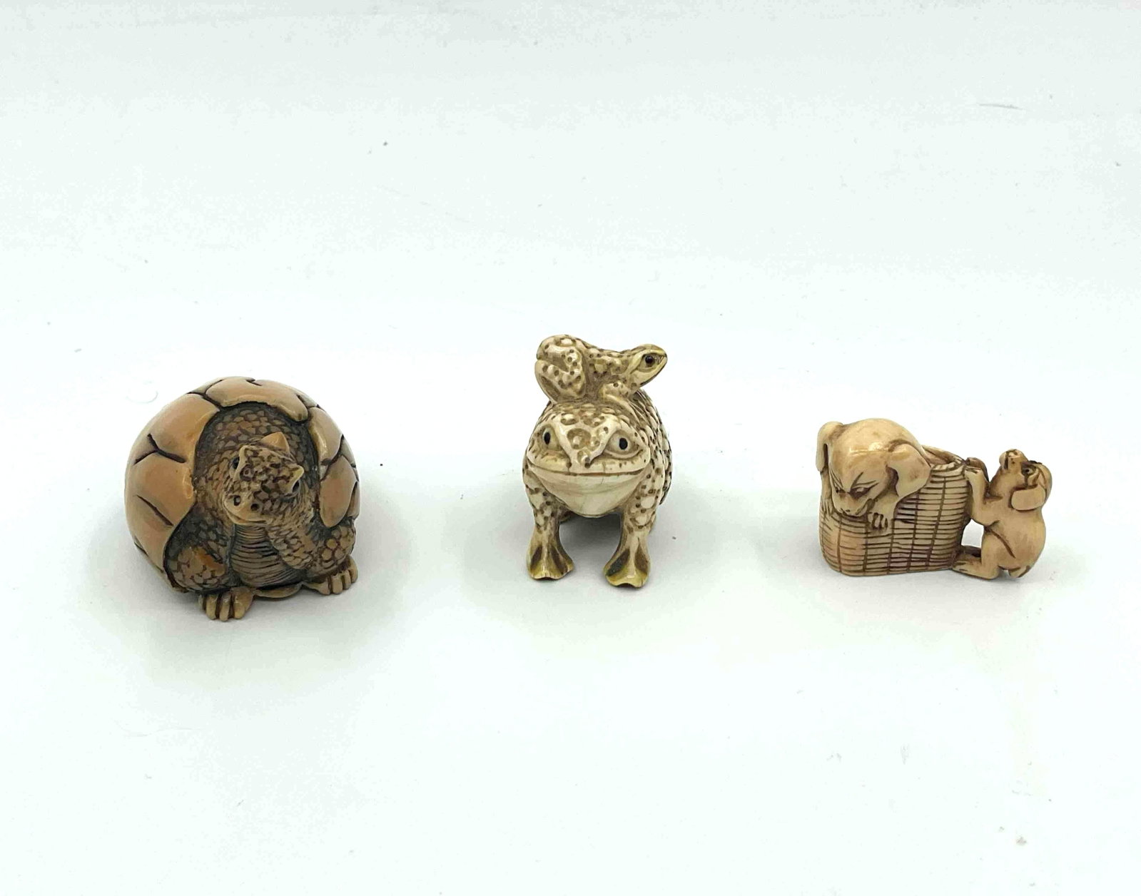 Three Japanese Style Netsuke Animal Figurines: Carved animal figures including a frog a turtle emerging from a cracked shell and a small animal on a platform likely crafted from resin or bone imitation material Medium Carved resin or composite mat