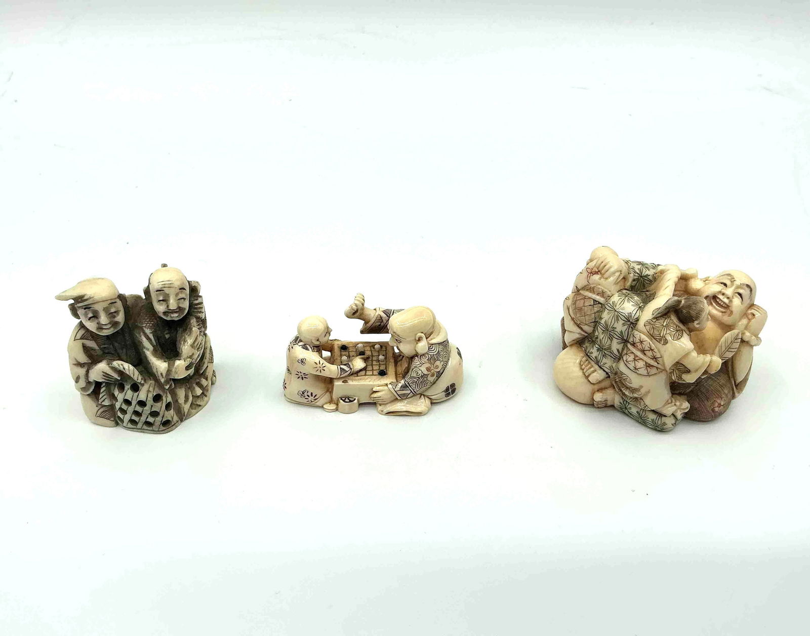 Three Japanese Style Netsuke Figurines: Group of small carved figures including a pair of standing figures a reclining figure and a seated figure holding an object likely crafted from resin or bone imitation material Medium Carved resin or