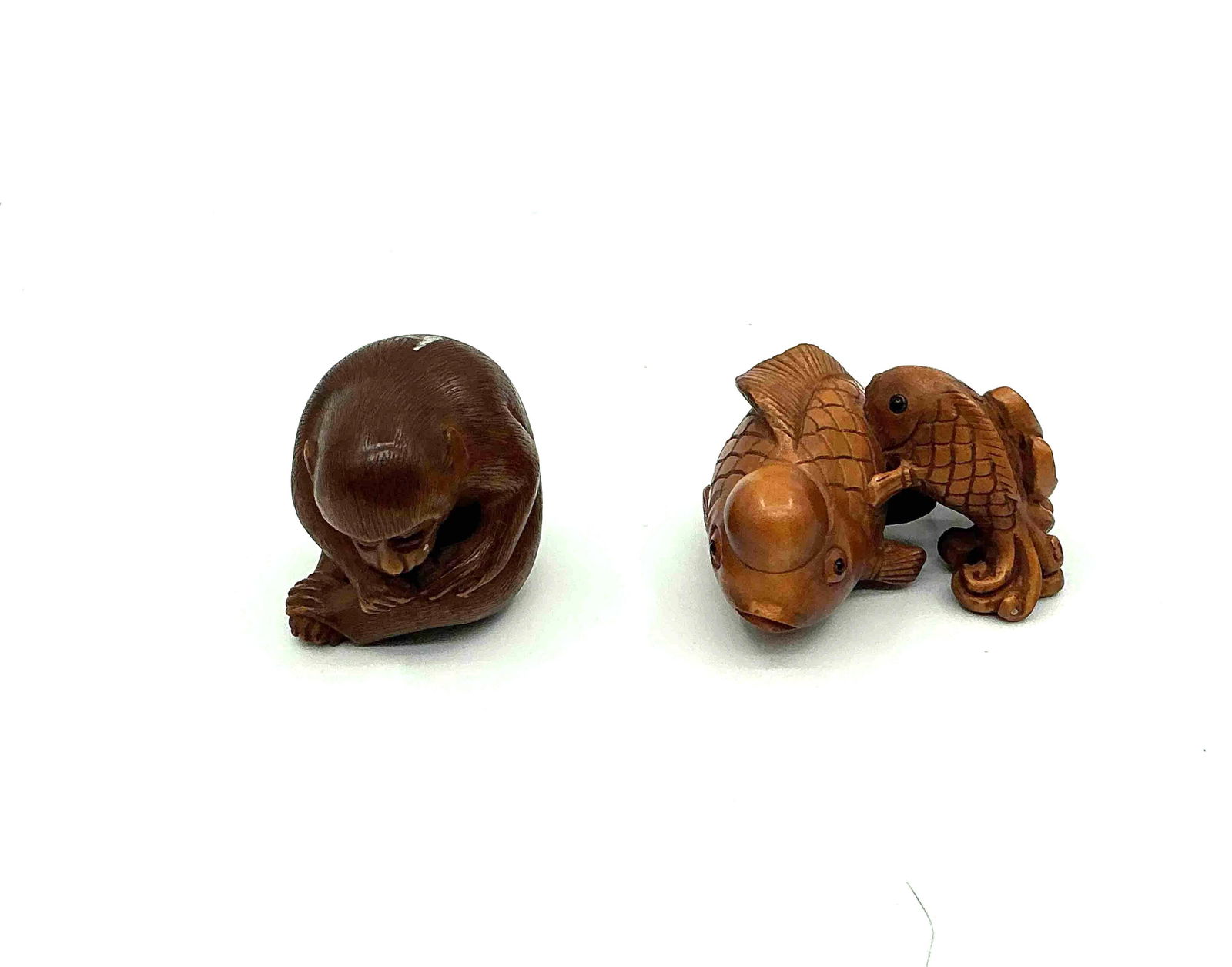 Japanese Style Netsuke Figurines: Two small carved figures in reclining or crouched positions likely representing traditional Japanese characters crafted from resin or bone imitation material Medium Carved resin or composite material