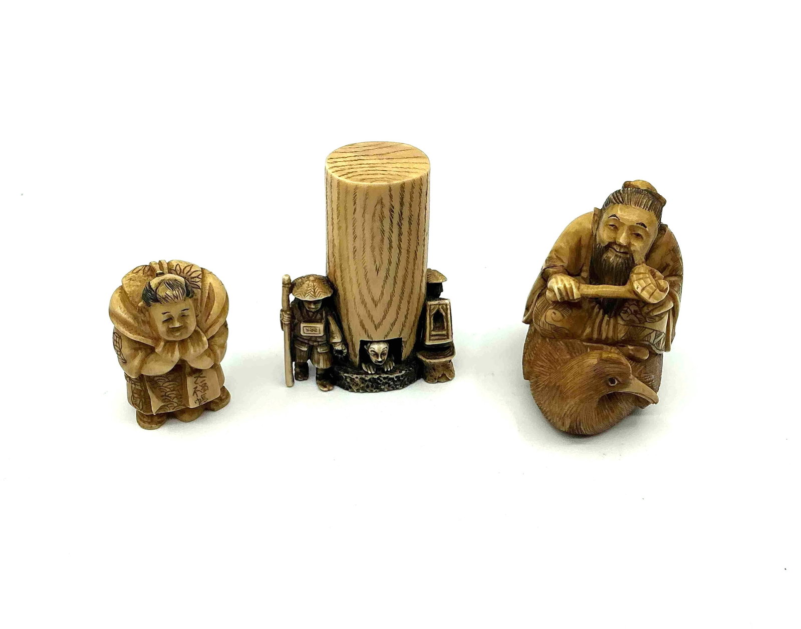 Three Japanese Style Netsuke Figurines: Group of small carved figures including a standing figure with hands together a drum or barrel piece and a seated figure holding an object likely crafted from resin or bone imitation material Medium C