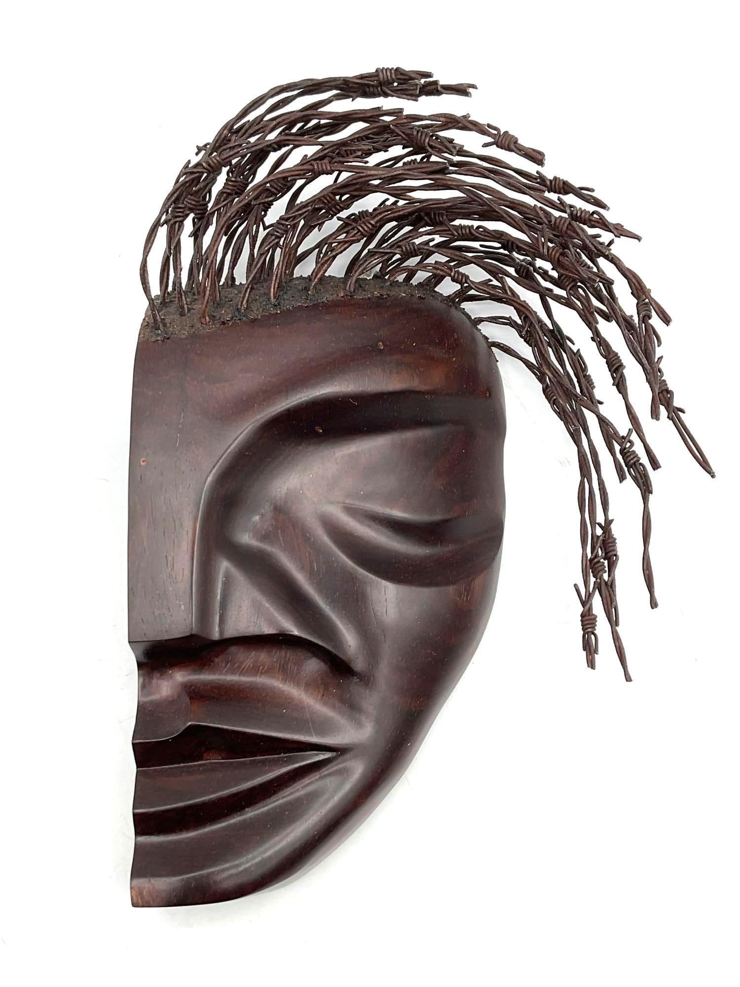 African carved face mask with wire hair detail: Stylized hand-carved wooden face mask featuring sharp geometric contours and coiled wire strands simulating hair. Dimensions: H12in L8in W4in Medium: Carved wood and twisted metal wire.