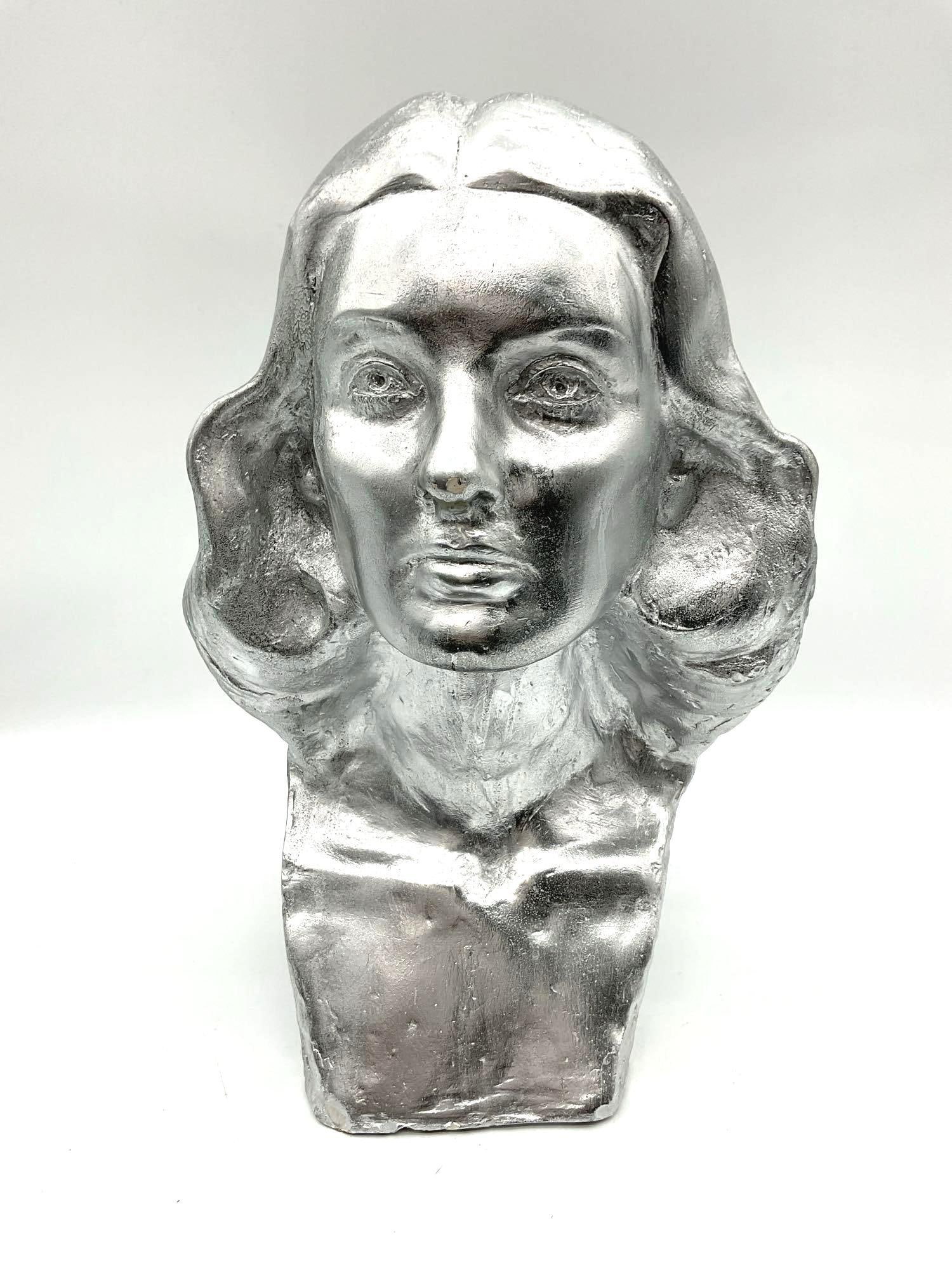 STEIN, Modest - Metallic Female Bust - 1956: Expressive sculptural bust of a woman, finished in a reflective silver metallic coating. The piece features stylized facial features and softly flowing hair, combining classical influence with a moder