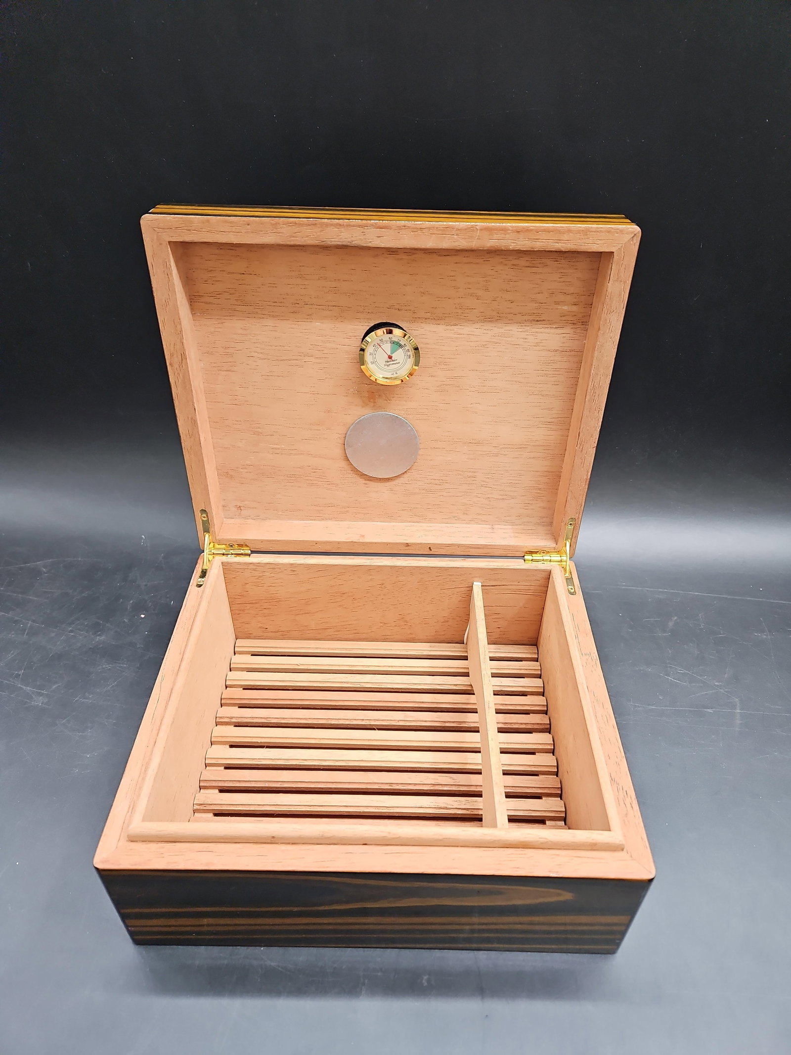 Humidor: A polished wooden humidor with a sleek finish, designed for cigar storage. The interior features a built-in hygrometer and humidity control system, ensuring optimal conditions for preserving cigars. T