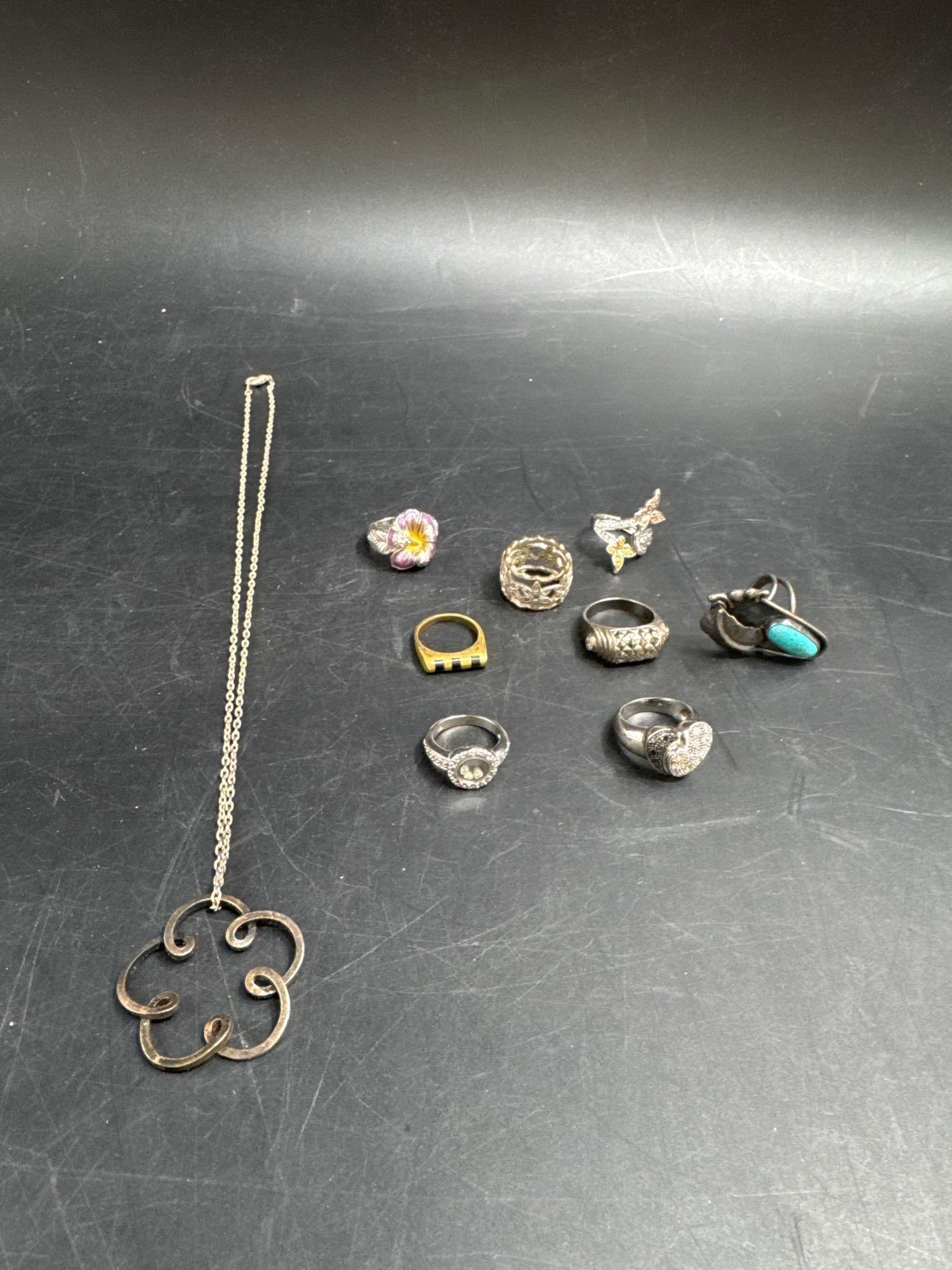 Assorted Vintage Jewelry Lot – Rings & Necklace: Collection of vintage jewelry including a large openwork pendant necklace and eight assorted rings. The rings feature a variety of designs such as floral enamel, turquoise stone, textured silver, hear