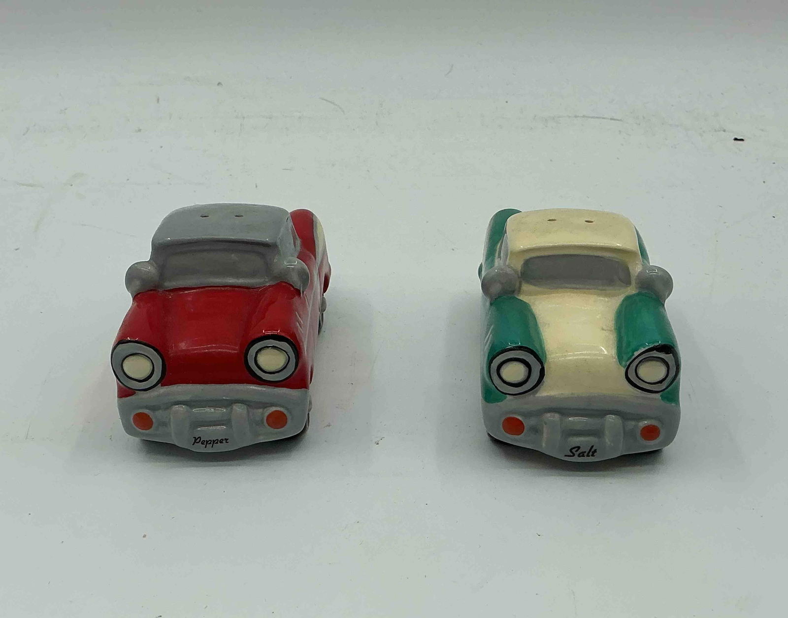 Vintage Car Salt and Pepper Shakers: Pair of ceramic novelty salt and pepper shakers in the shape of classic cars, one in turquoise with cream accents and the other in red with gray accents. Playful collectible set, ideal for kitchen or