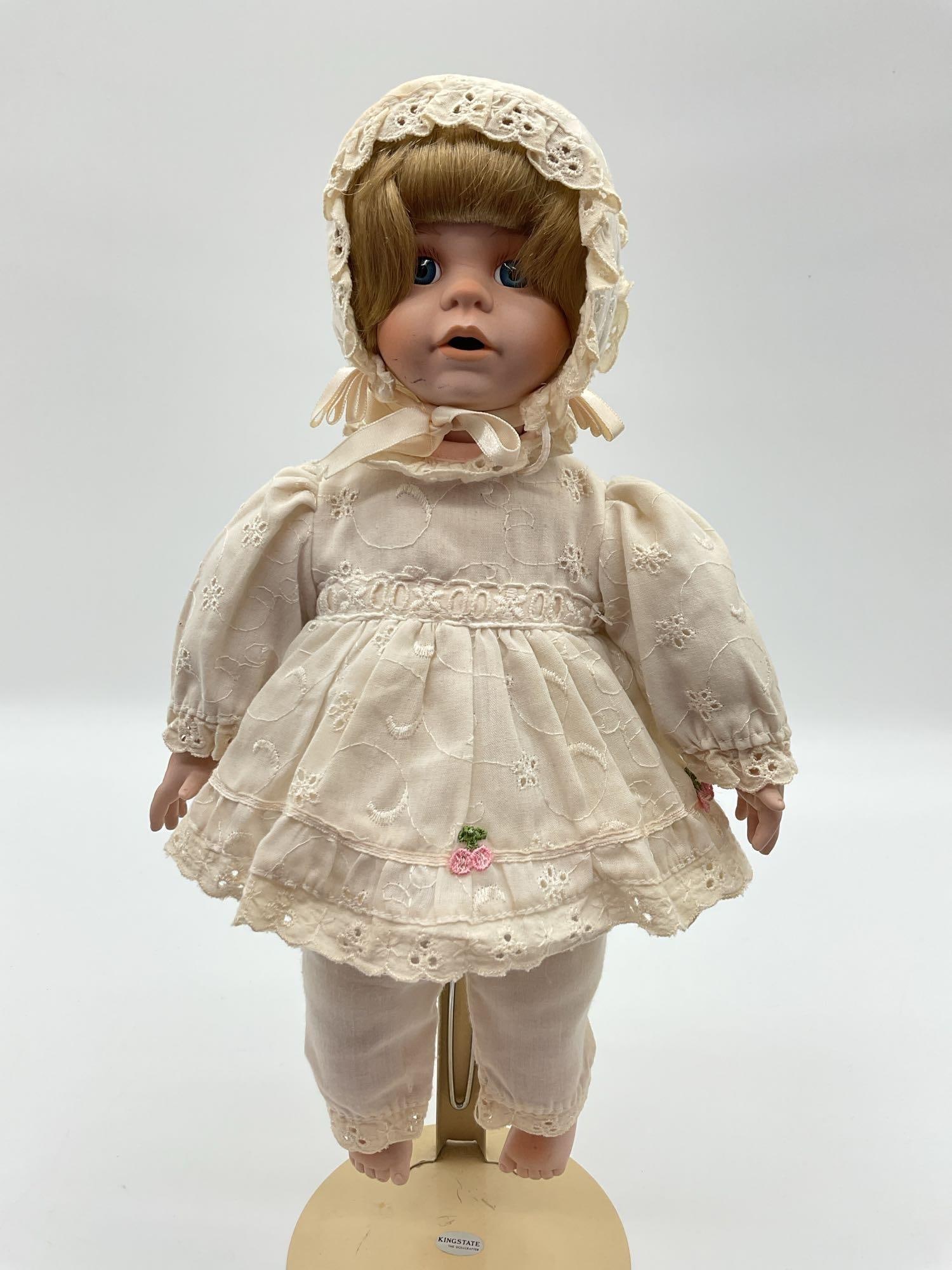 Antique-Style Porcelain Baby Doll in White Lace Outfit: This vintage or antique-style porcelain baby doll is dressed in an all-white lace-trimmed outfit, including a bonnet, a ruffled top, and matching bloomers with small pink floral embroidery. She has br