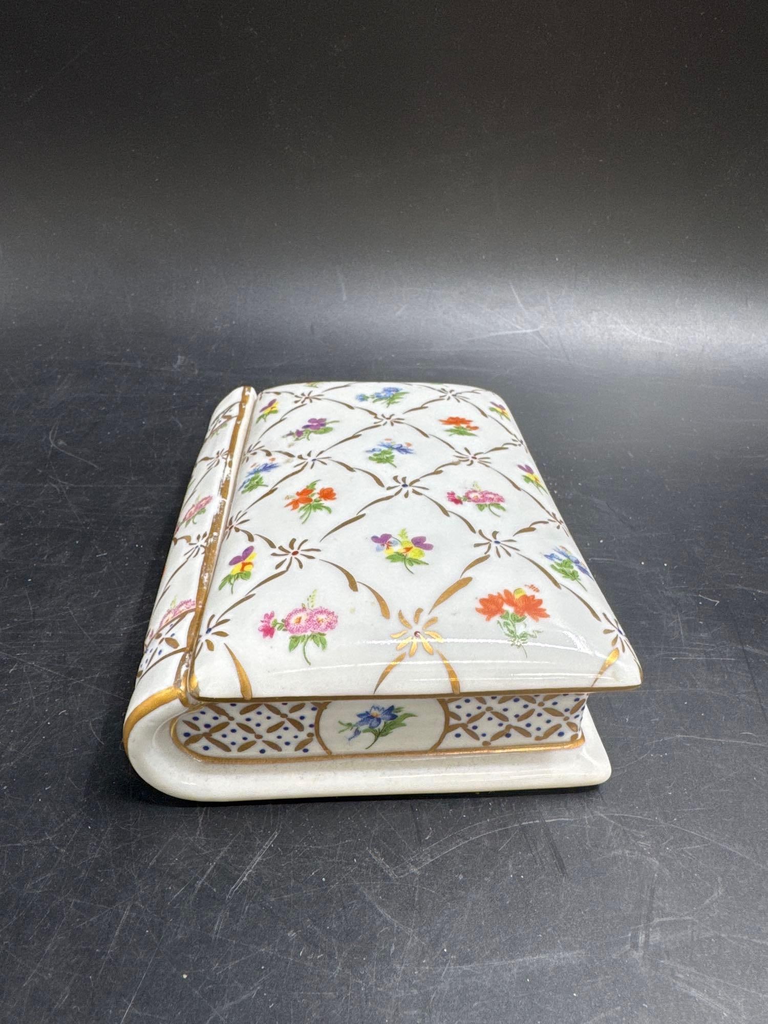 Antique Porcelain Book-Shaped Trinket Box: Unique porcelain trinket box crafted in the shape of a closed book, decorated with delicate floral sprays in multicolor against a white ground. The lid lifts to reveal a rectangular compartment for sm
