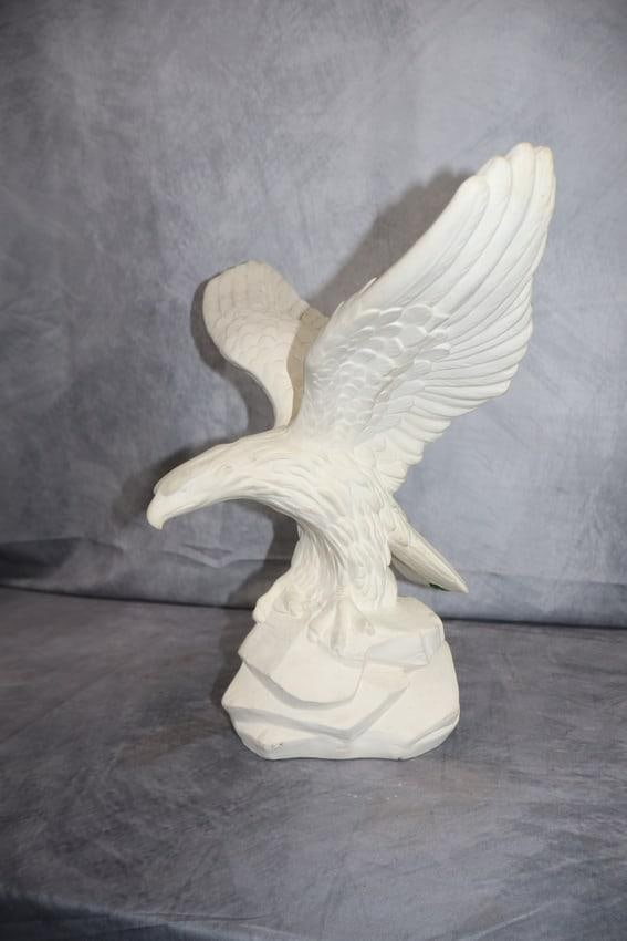 White Bisque Eagle: A stylized white ceramic sculpture of an eagle in mid-flight, wings fully spread as it prepares to land on a rocky base. The piece is unglazed, giving it a matte finish and highlighting the detailed f