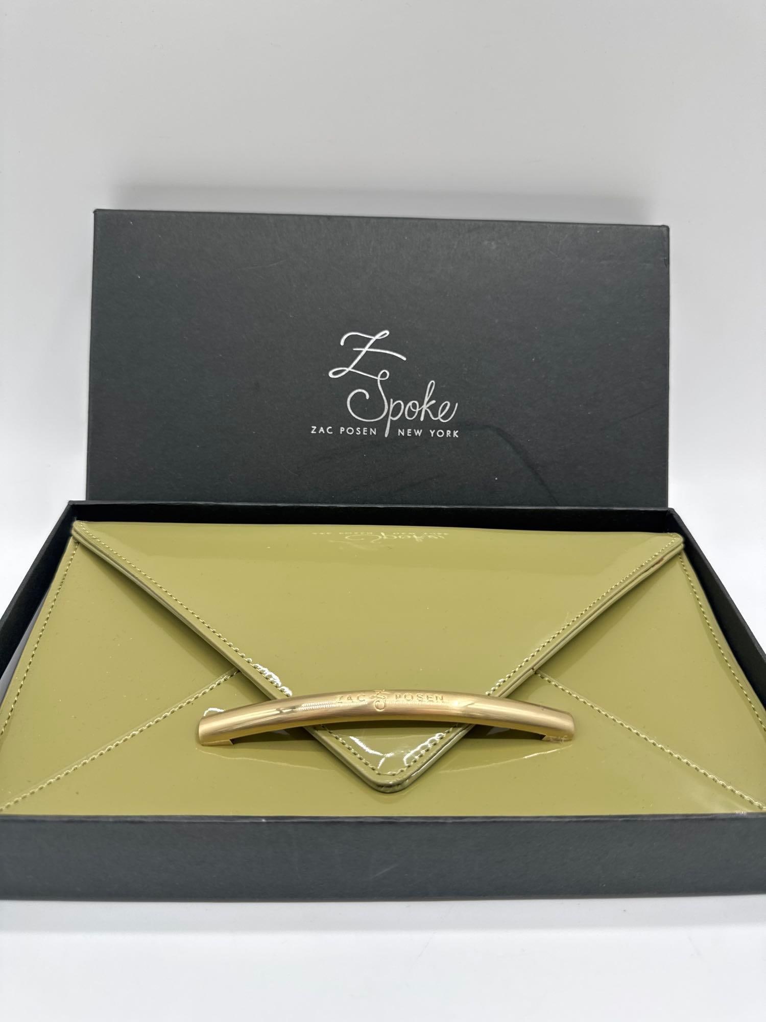 Z Spoke Zac Posen Patent Leather Clutch: Designer clutch by Zac Posen’s Z Spoke line, crafted in glossy olive green patent leather with an envelope-style flap. Features a gold-tone bar engraved with “Zac Posen.” Comes with original
