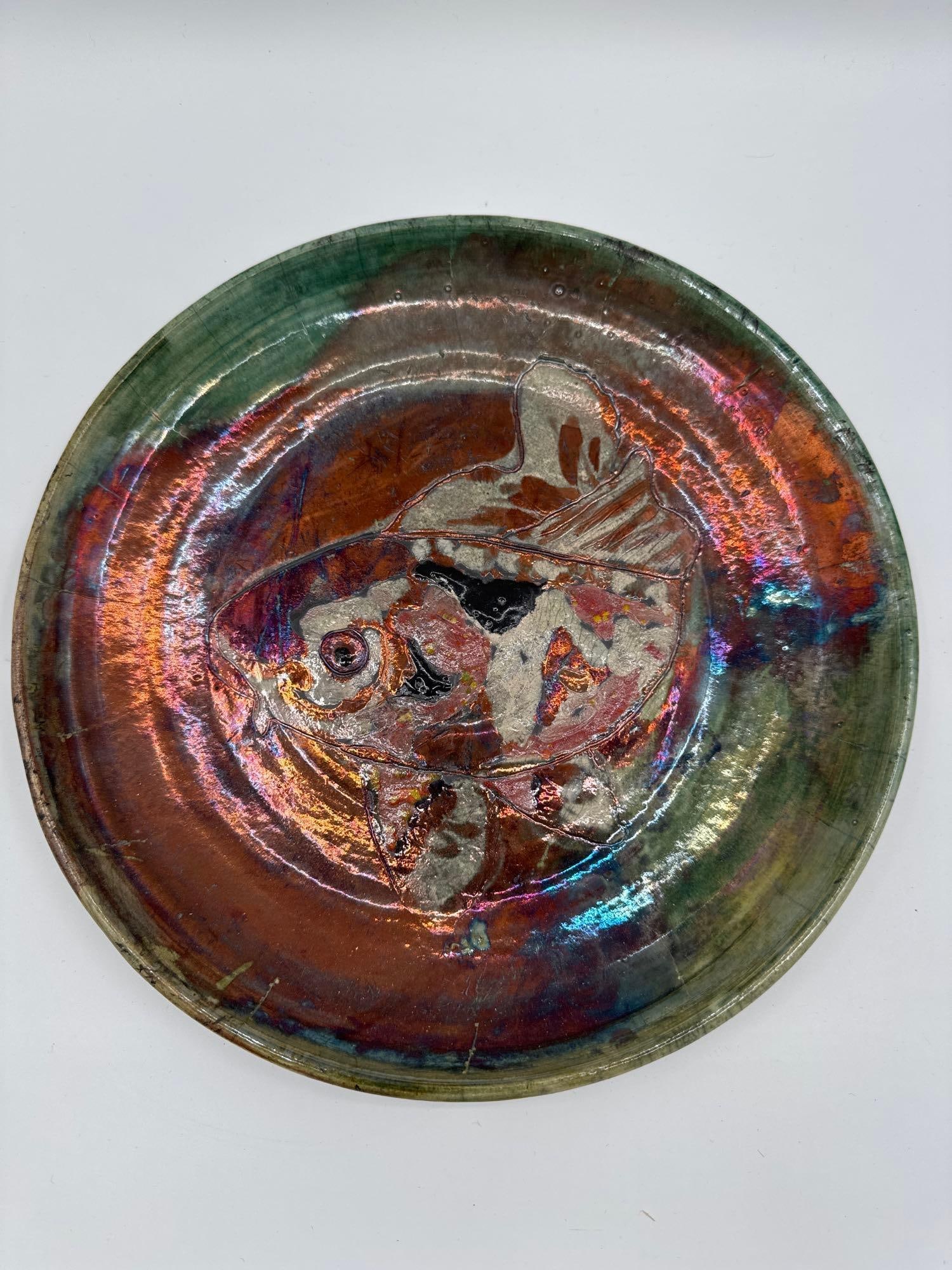 Iridescent Fish Plate by Michael Cordray: High-fired functional pottery plate featuring a stylized fish design with striking raku-style luster glaze in multicolor hues. Medium: Wheel-thrown ceramic with raku ware glaze, lead-free, dishwasher