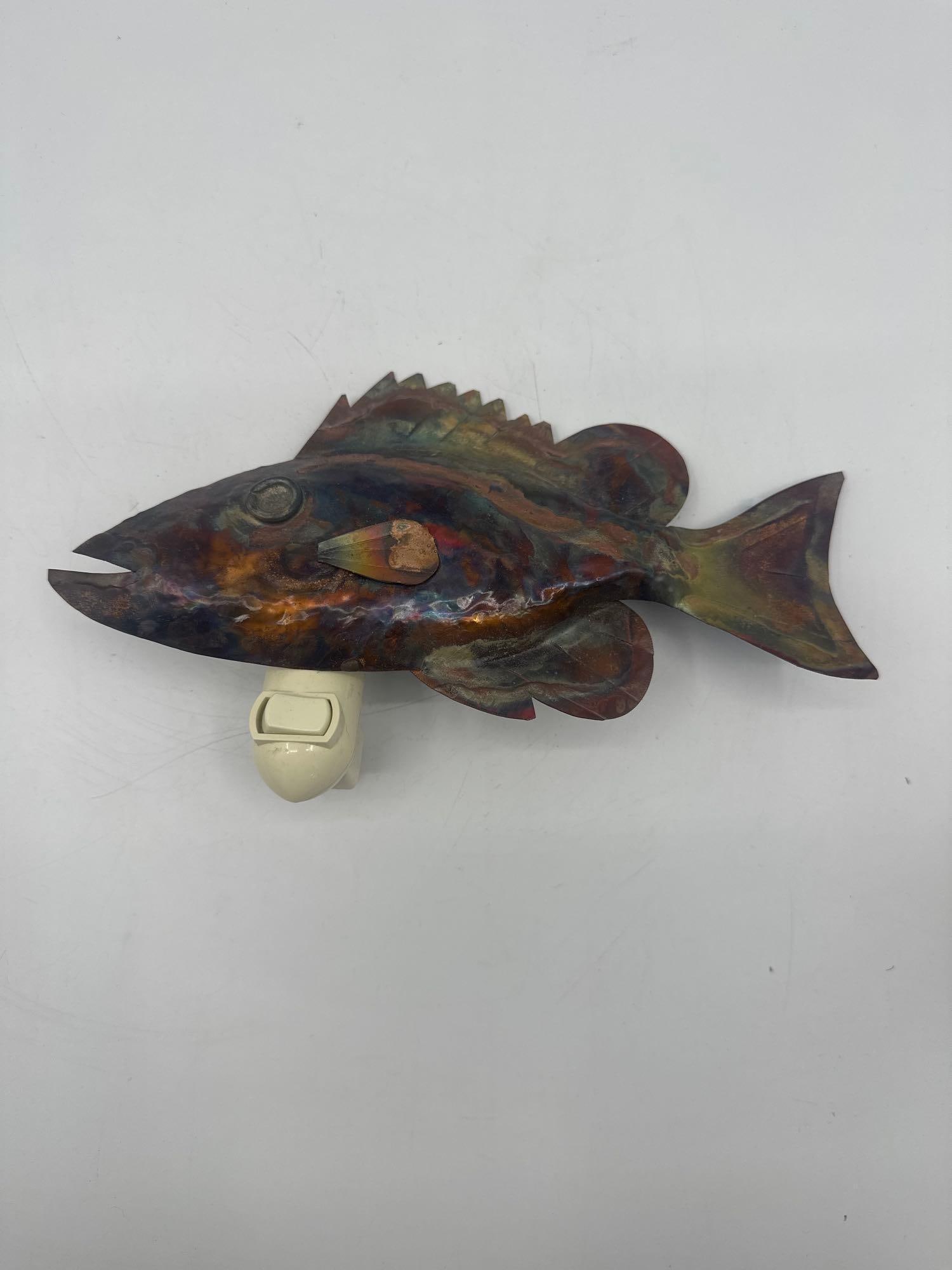 Handcrafted Metal Fish Night Light by Jenkins: A whimsical night light featuring a hand-shaped fish form made from heat-treated, patinated metal. The vibrant iridescent finish displays fiery blues, oranges, and purples. Signed "Jenkins" on