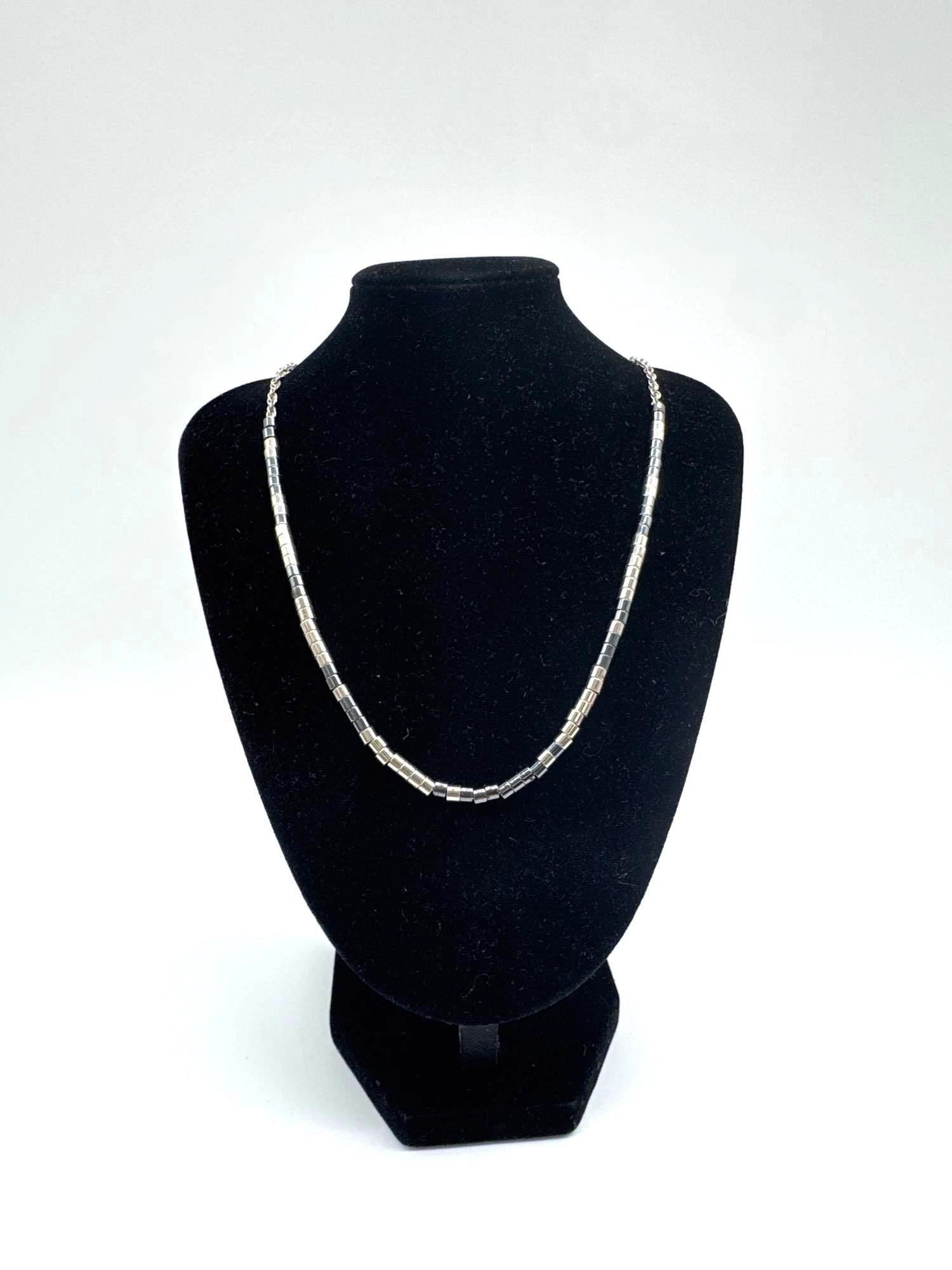 Sterling Silver Cylinder Bead Necklace: Simple and elegant necklace featuring evenly spaced cylindrical sterling silver beads, strung together in a minimalist design. Displayed on a black jewelry stand. Medium Sterling silver beaded necklac