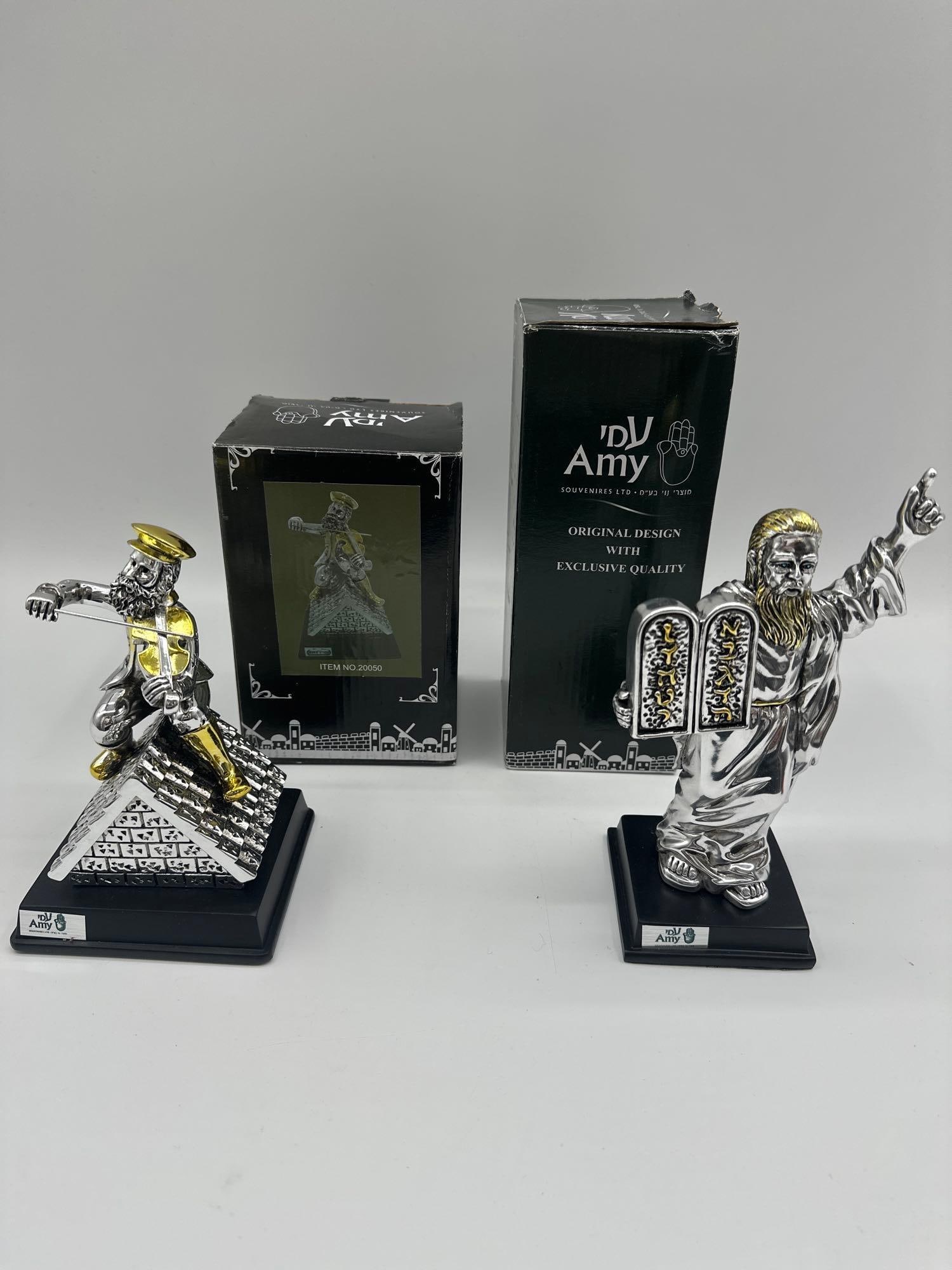 Silver and Gold Tone Judaica Figurines by Amy Sterling Clad & Gilt Fiddler on the Roff: Set of two polished silver-tone resin figurines with gold accents. One depicts a violinist on a rooftop, referencing the Fiddler on the Roof. The other shows Moses holding the Ten Commandments. Medium