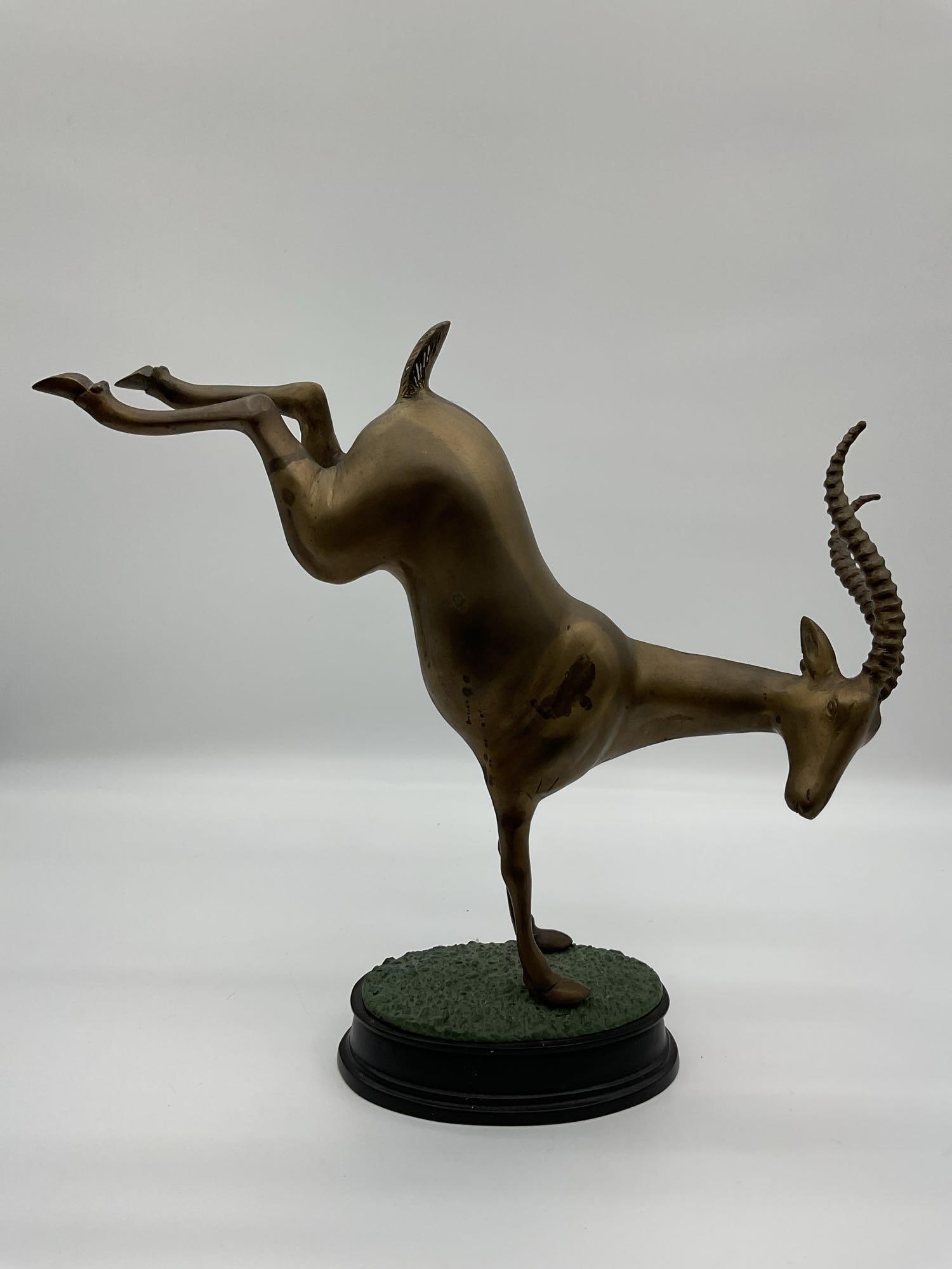 Handstand Antelope Bronze Sculpture: Whimsical brass sculpture of an antelope balancing on its front legs, mounted on a green and black oval base. Dimensions: H17in L20in W4in Medium: brass on composite base