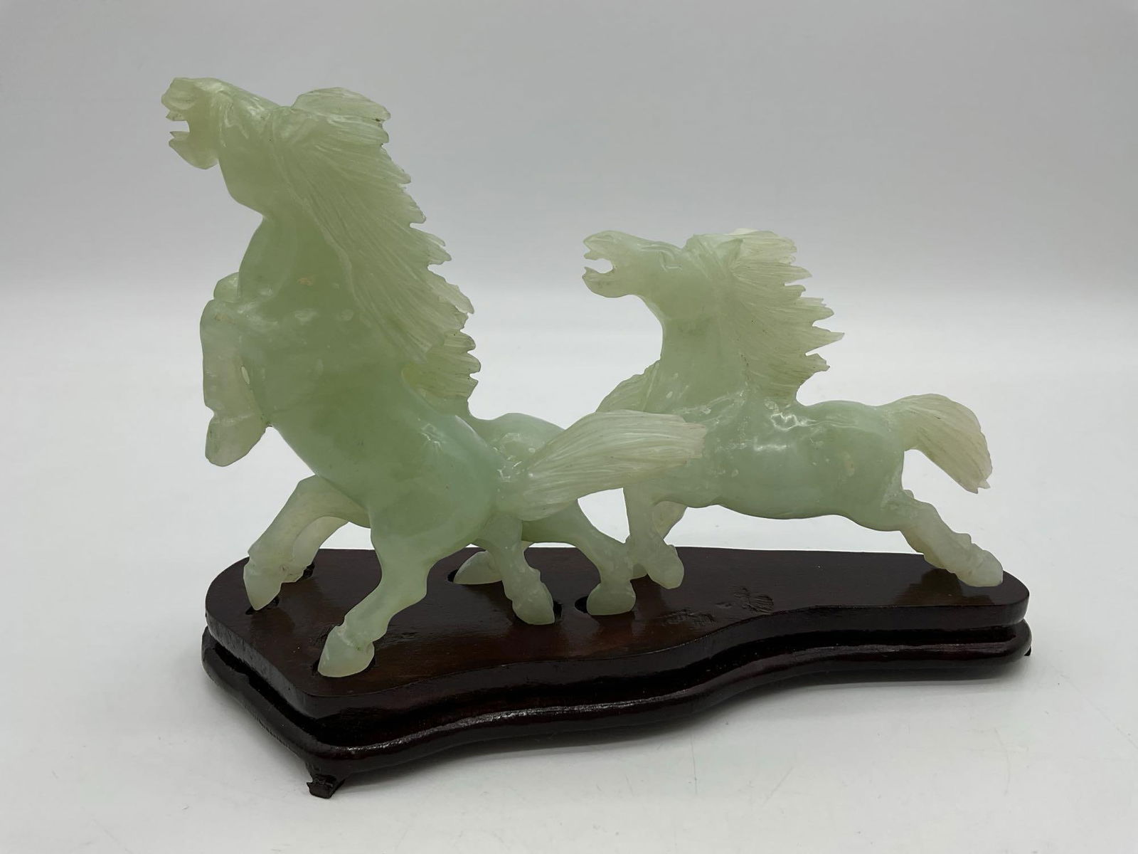 Trio of Jade Horses: Hand-carved green jade sculpture featuring three galloping horses on a wooden base, symbolizing strength and success in traditional Chinese culture. Dimensions: H7in L9in W3in Medium: Jade stone with