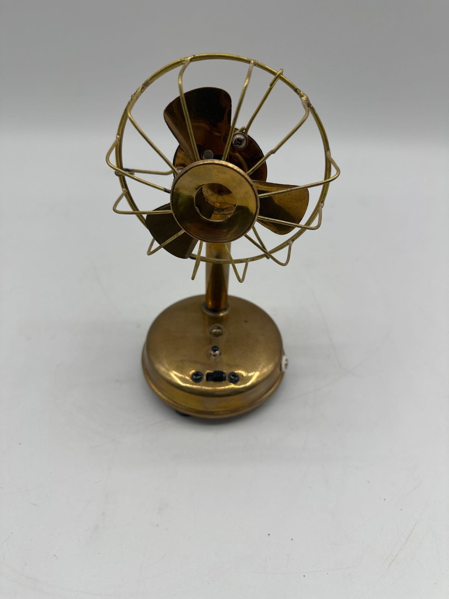 Vintage Brass Miniature Electric Fan: A small decorative fan crafted from brass with a three-blade propeller encased in a metal cage. The base features a switch and light indicator, suggesting it may function as a novelty or USB-powered f
