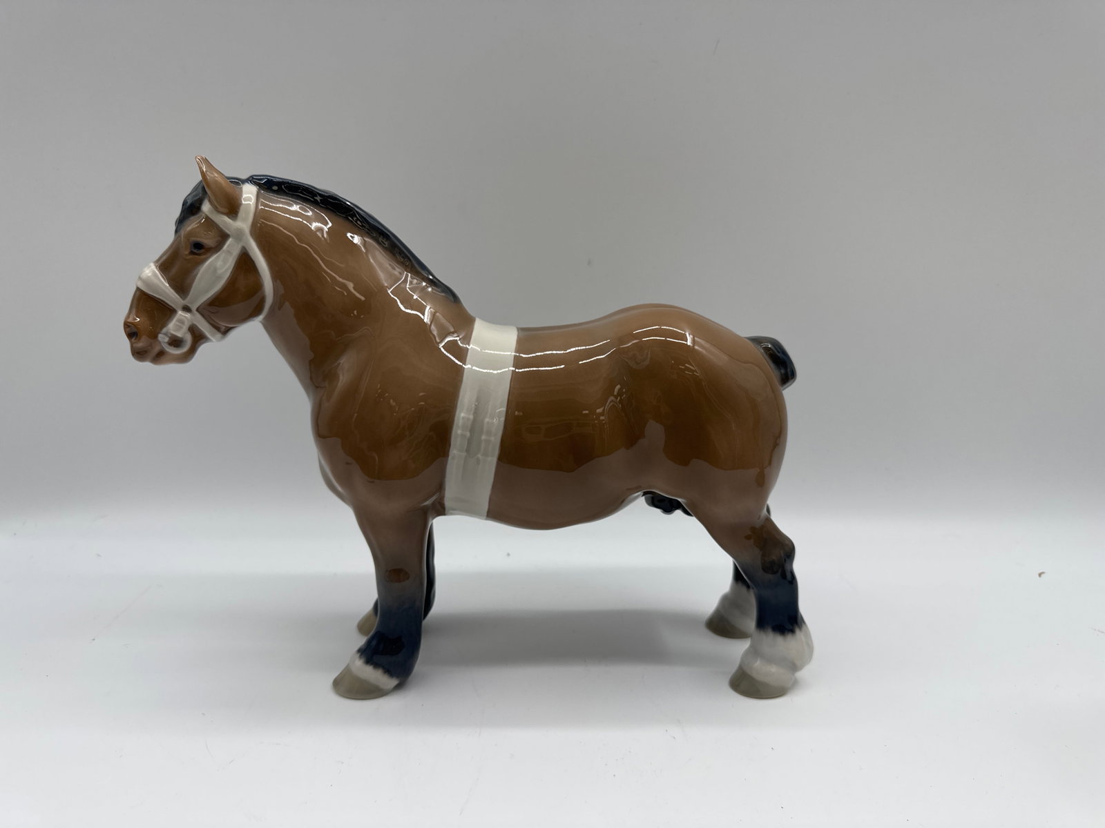 Bing & Grondahl Porcelain Horse "Belgian Stallion": Porcelain figurine of a brown horse with white harness. Marked on the underside. Measures approximately 8 inches long.
